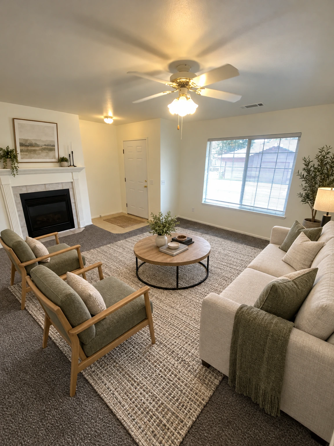 An empty room has gray carpet, a fireplace, a ceiling fan with lights, a closed door, and a window with blinds. (virtually staged)