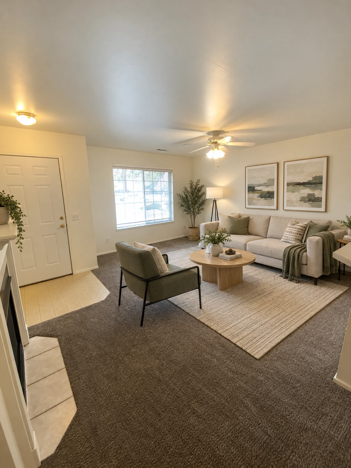 An empty room with gray carpet, a window with blinds, a white door, and a ceiling fan with lights. (virtually staged)