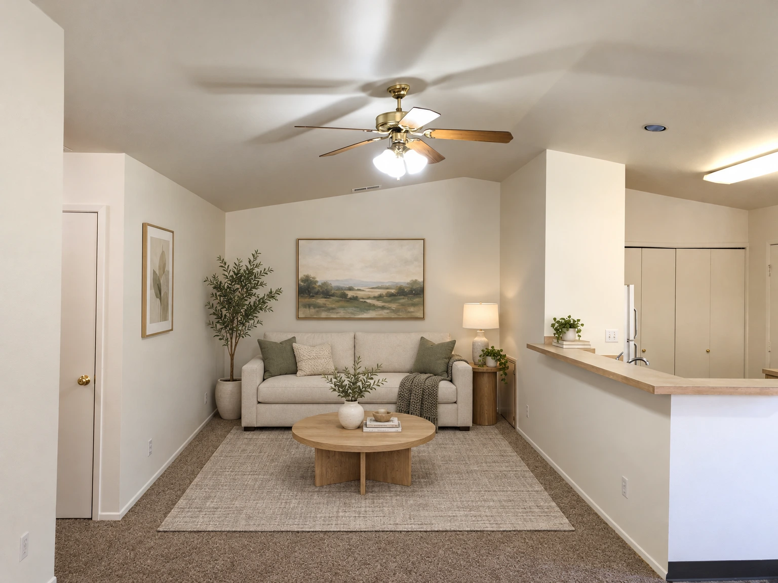An empty carpeted room with a ceiling fan and light, a closed door, and a kitchen counter with cabinets. (virtually staged)