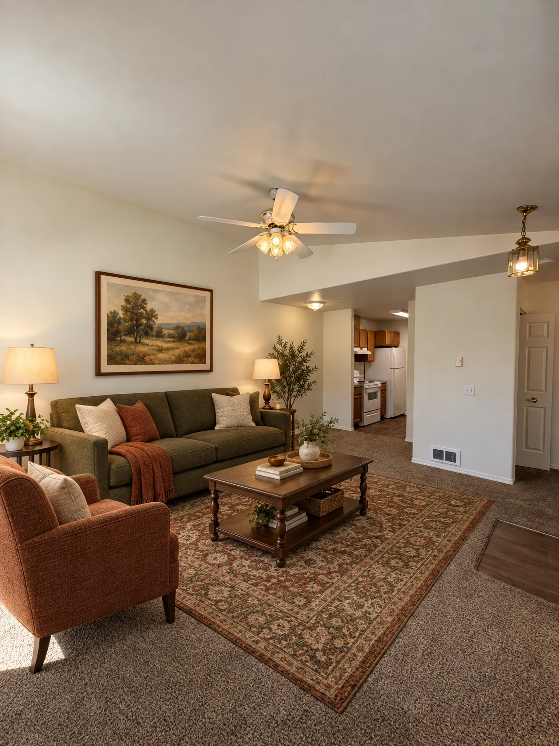 Carpeted room with a ceiling fan and lit fixtures, opening to a kitchen with wooden cabinets and white appliances. (virtually staged)