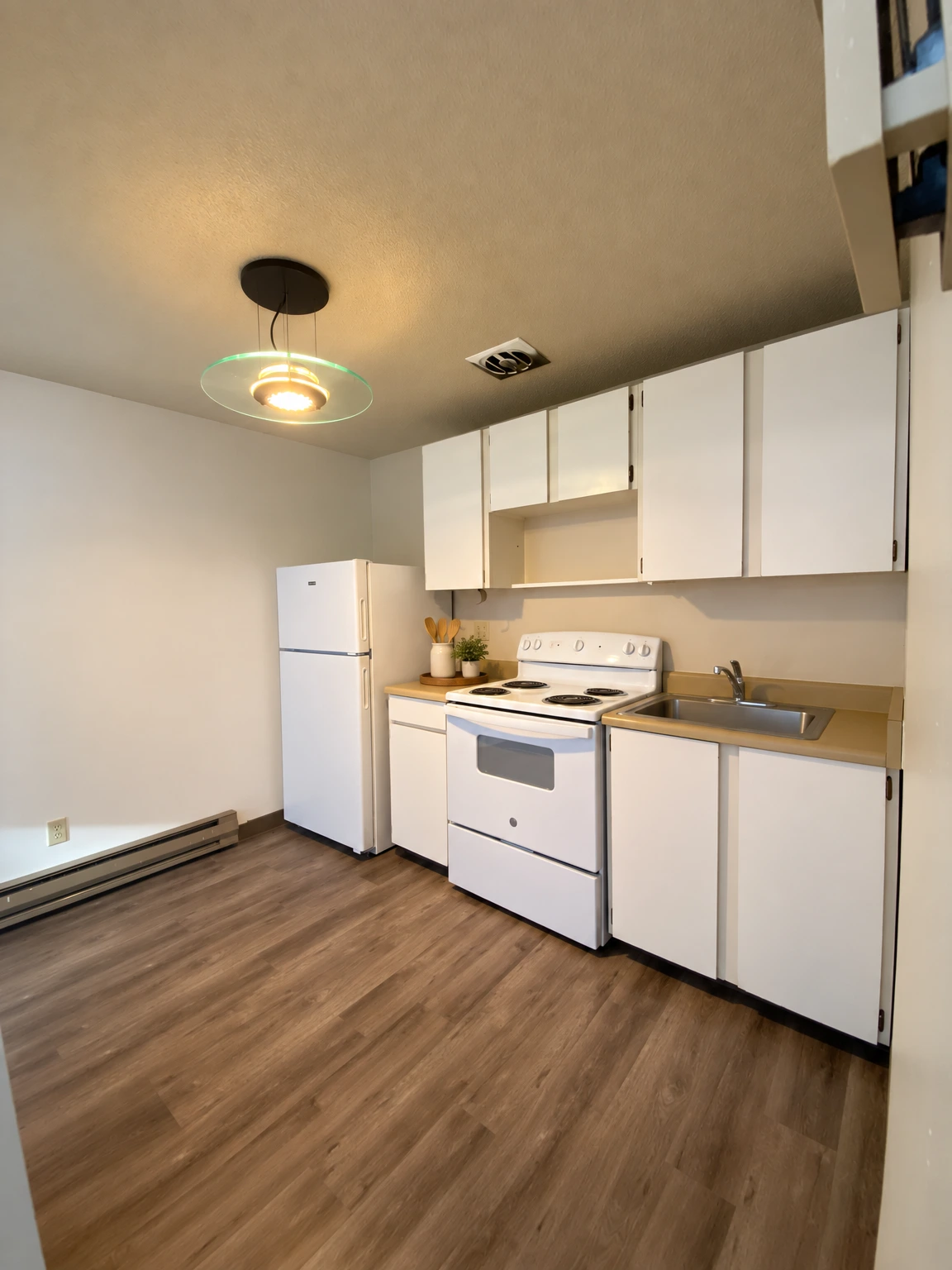 A small kitchen with white cabinets, a refrigerator, an electric stove, a sink, and a lit ceiling fixture. (virtually staged)