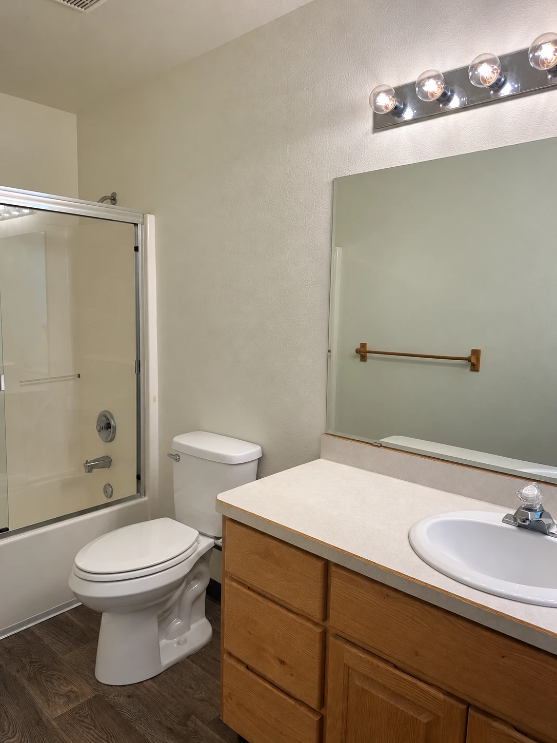 A bathroom with a glass shower enclosure, toilet, and wood vanity with a sink beneath a large mirror.