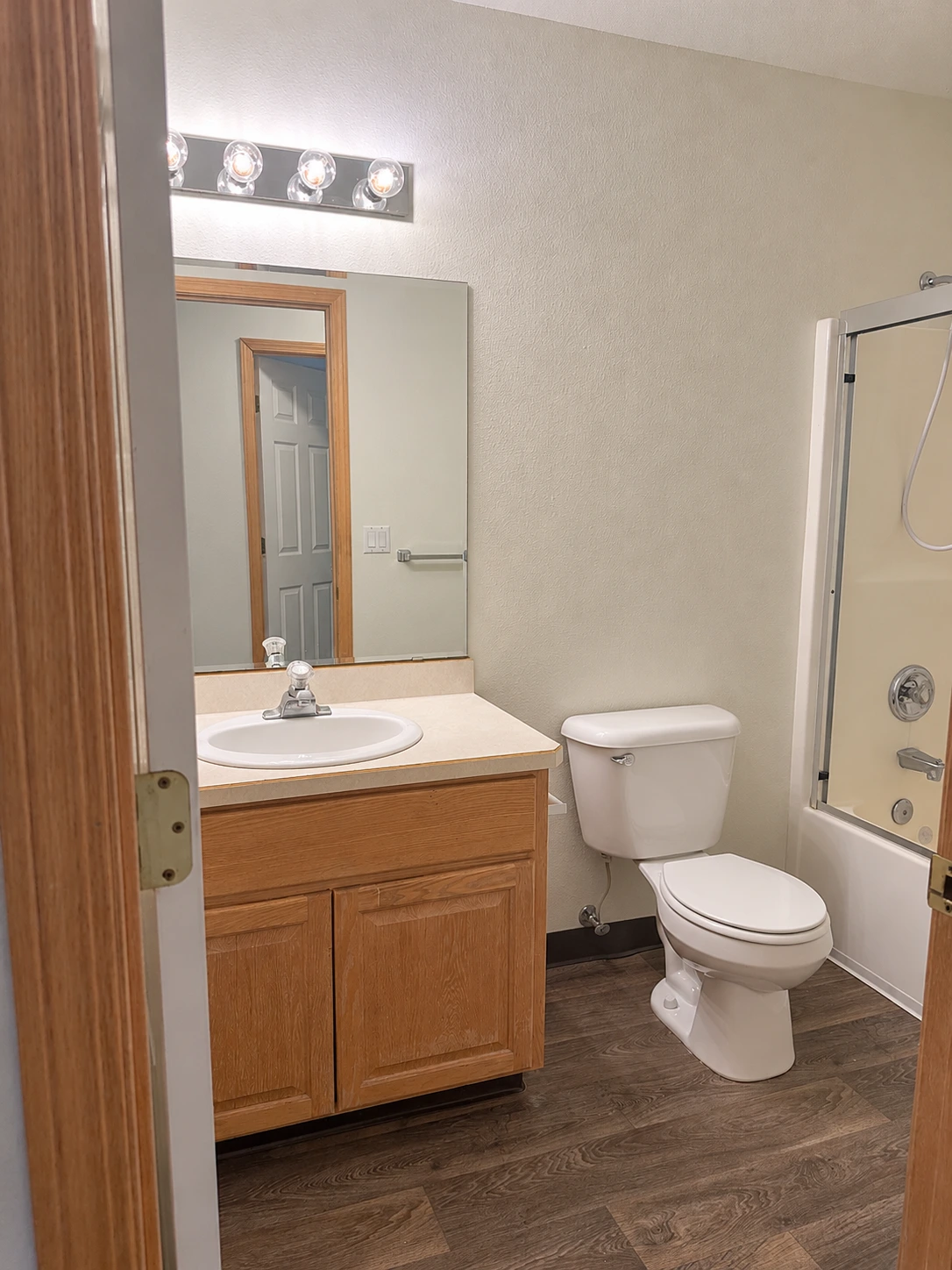 A bathroom with a wood vanity, oval sink, large mirror, toilet, and glass shower enclosure.