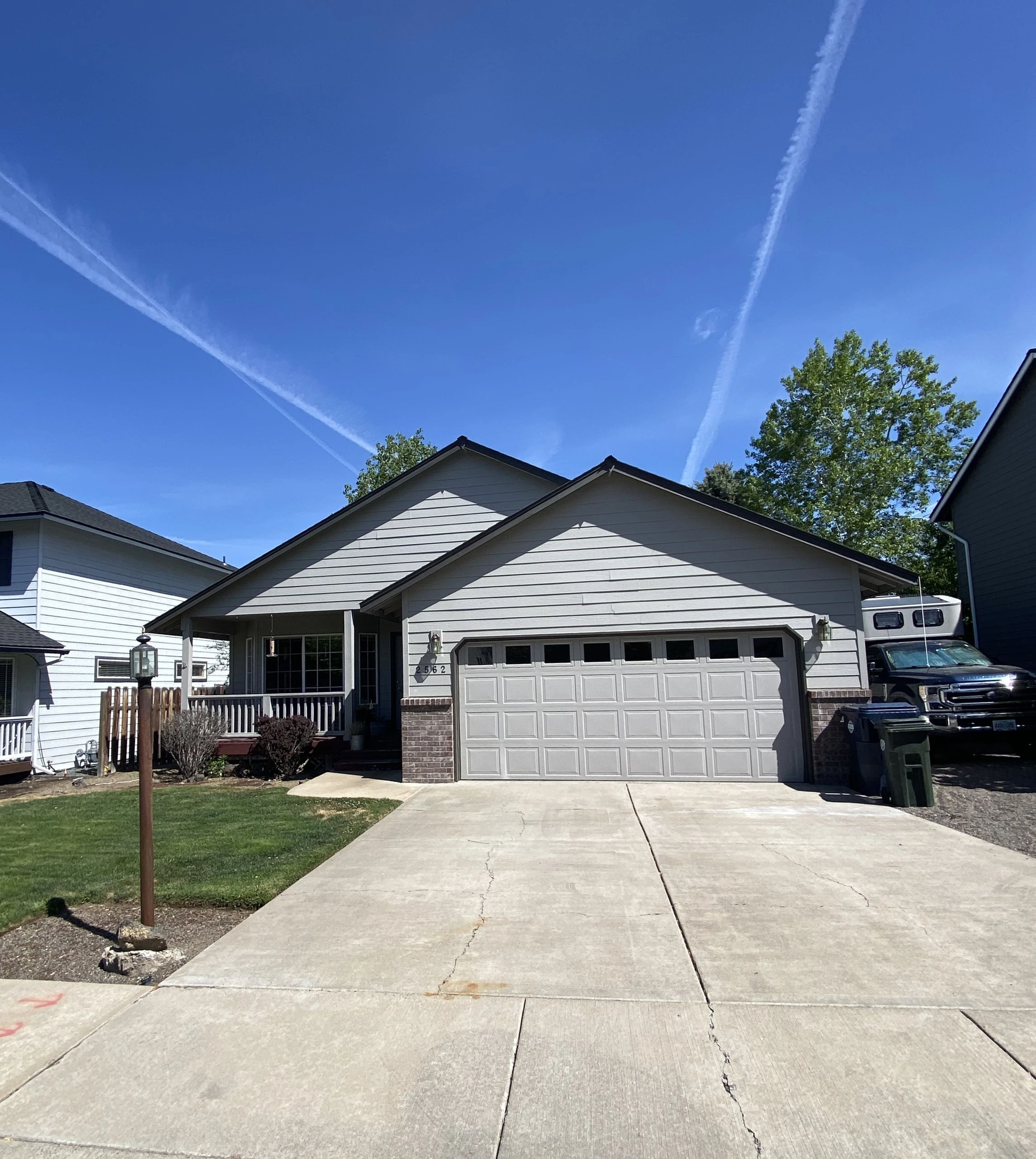 A gray house with a gabled roof, front porch, and paneled garage door stands beneath a blue sky with white streaks.