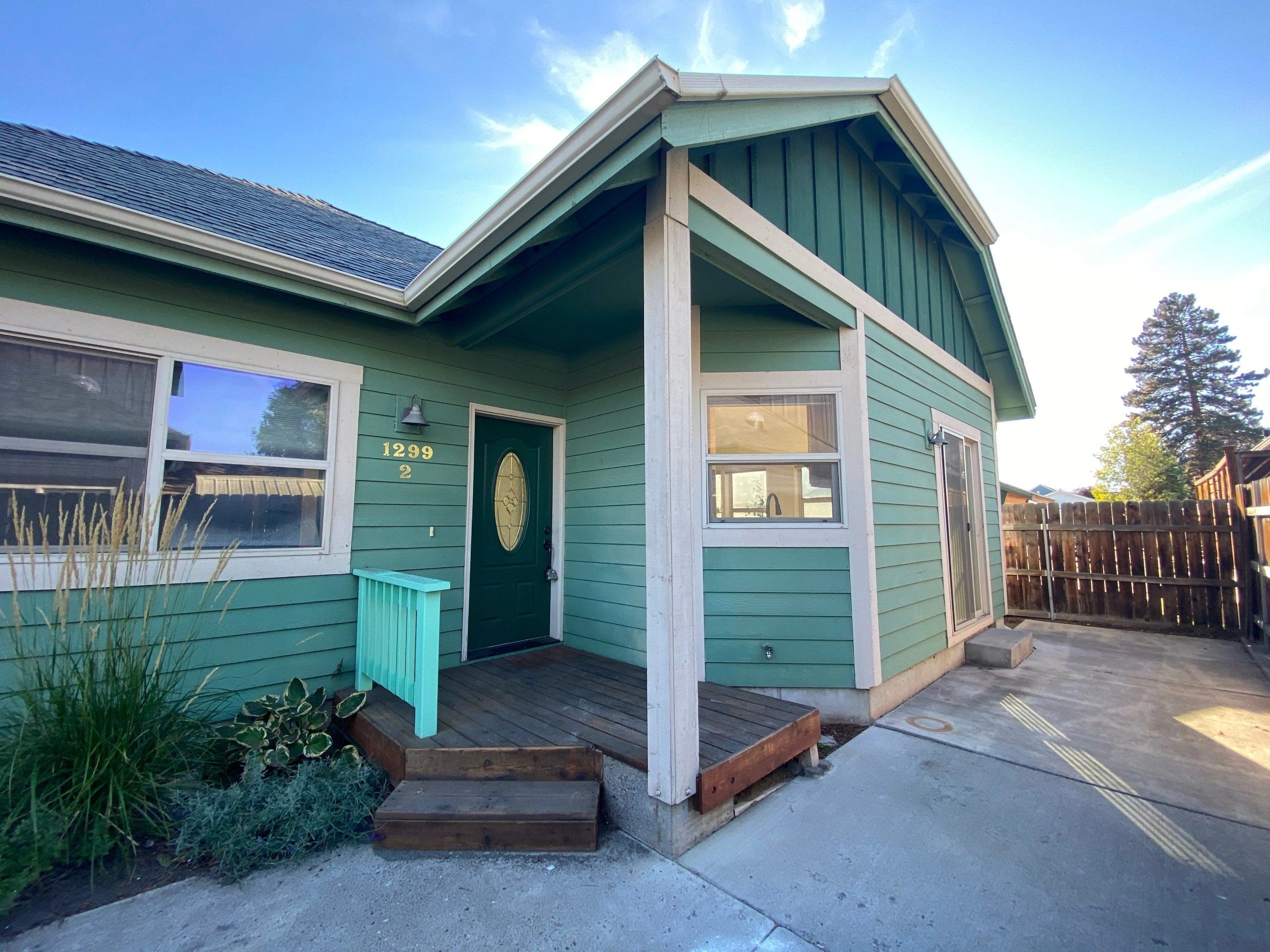 A teal-sided house has a covered wooden porch, dark front door, white trim, and several windows.