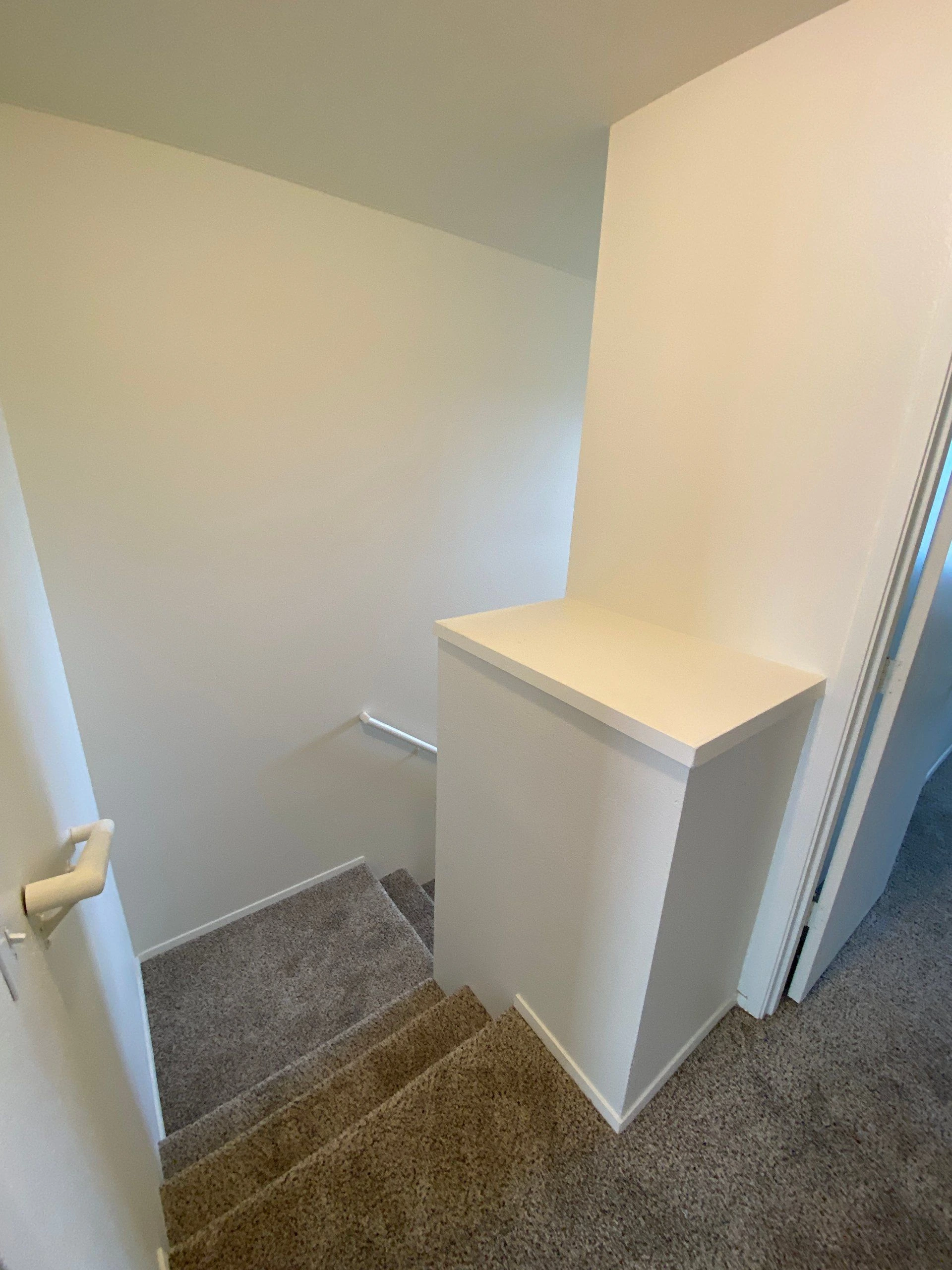Carpeted stairs descend beside a white half-wall with a flat ledge; an open door is visible at left.