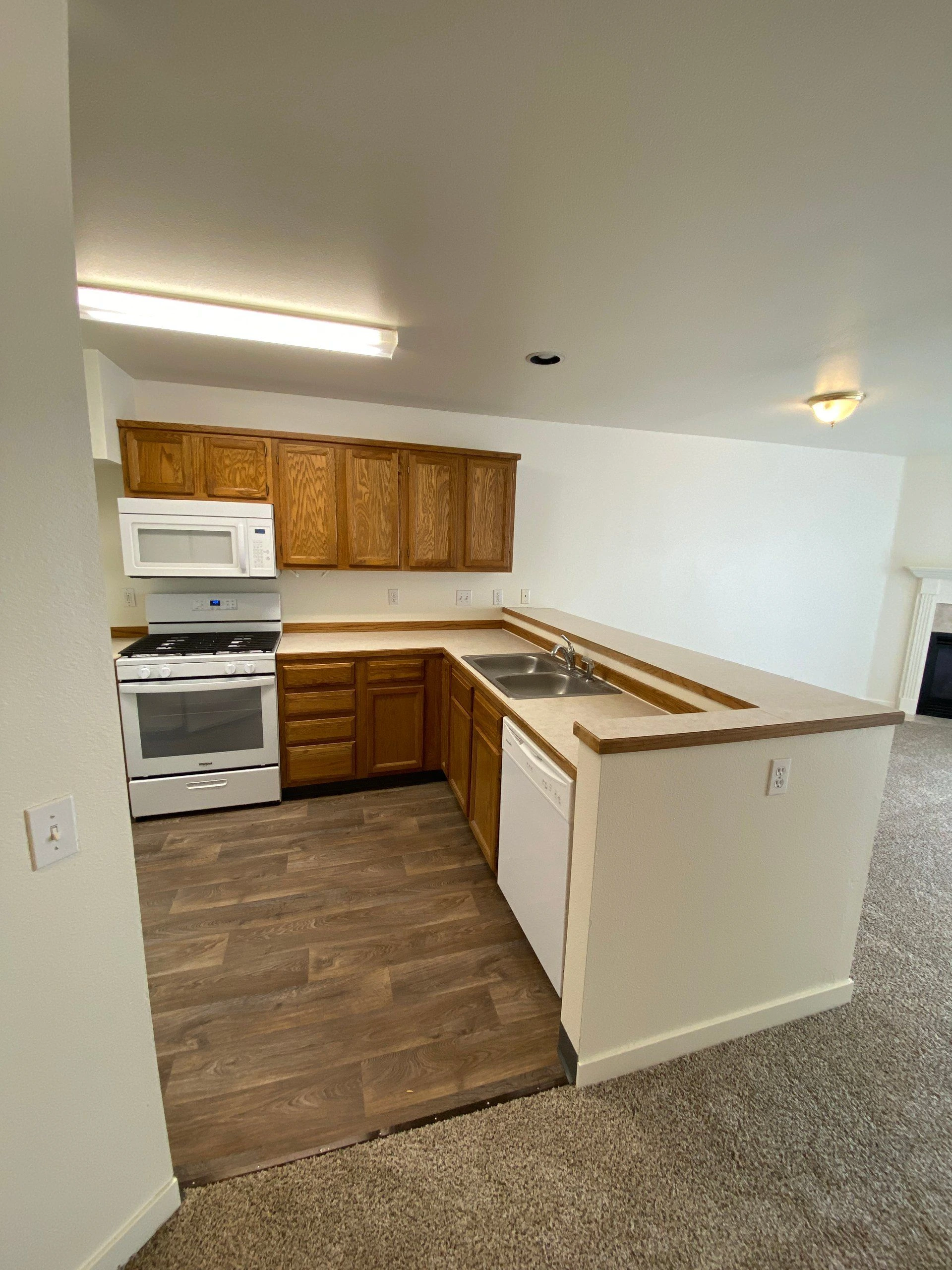 A kitchen with wood cabinets, a white range and microwave, a double sink, and an L-shaped counter.