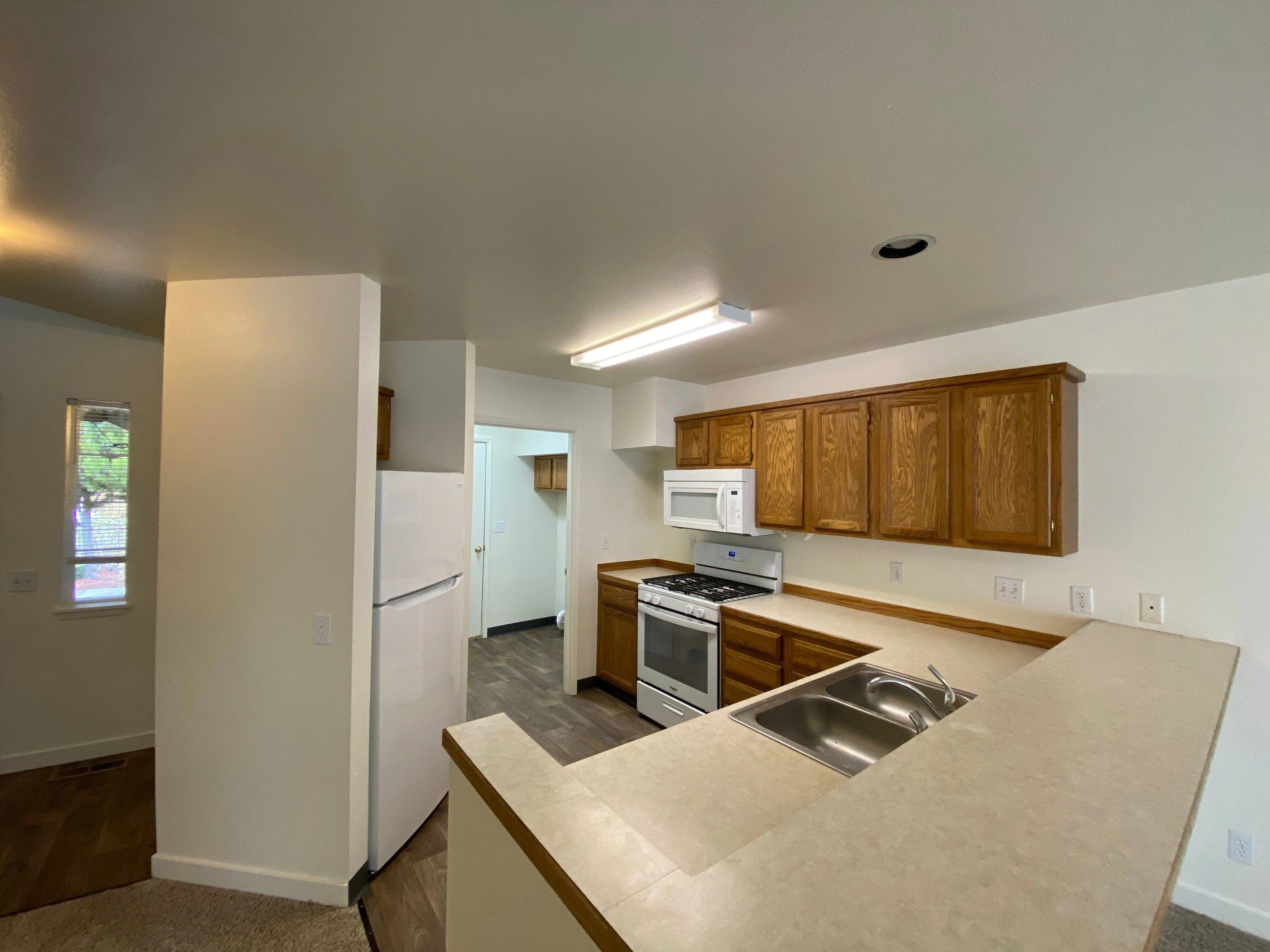 A kitchen with wood cabinets, a white refrigerator, microwave and stove, and a peninsula with a double sink.