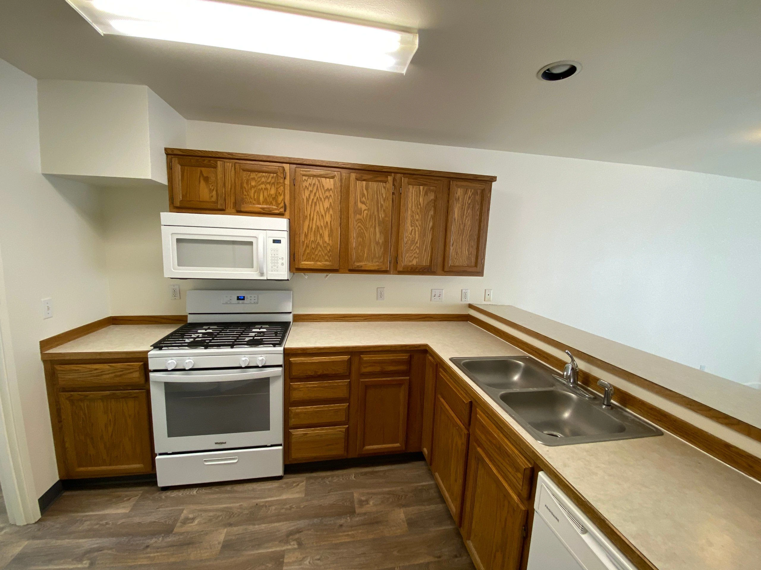 Kitchen with wood cabinets, light countertops, a range and microwave, and a double-basin sink.