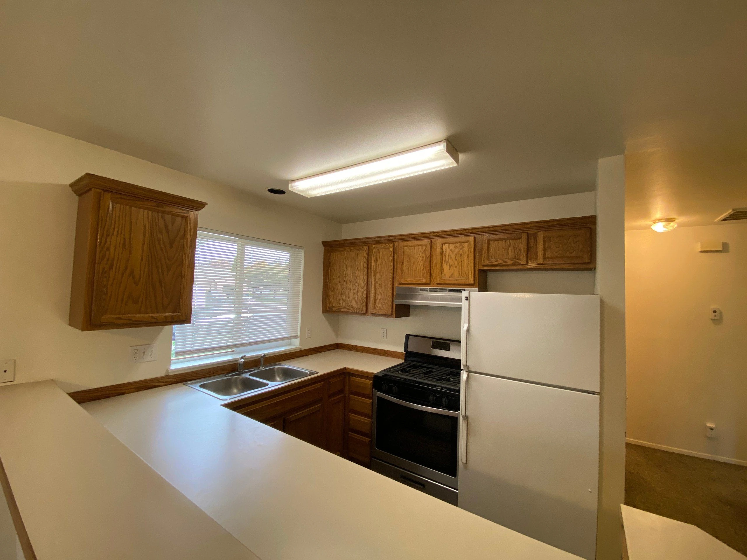 A kitchen with wooden cabinets, a double sink beneath a window, a gas range, and a white refrigerator.