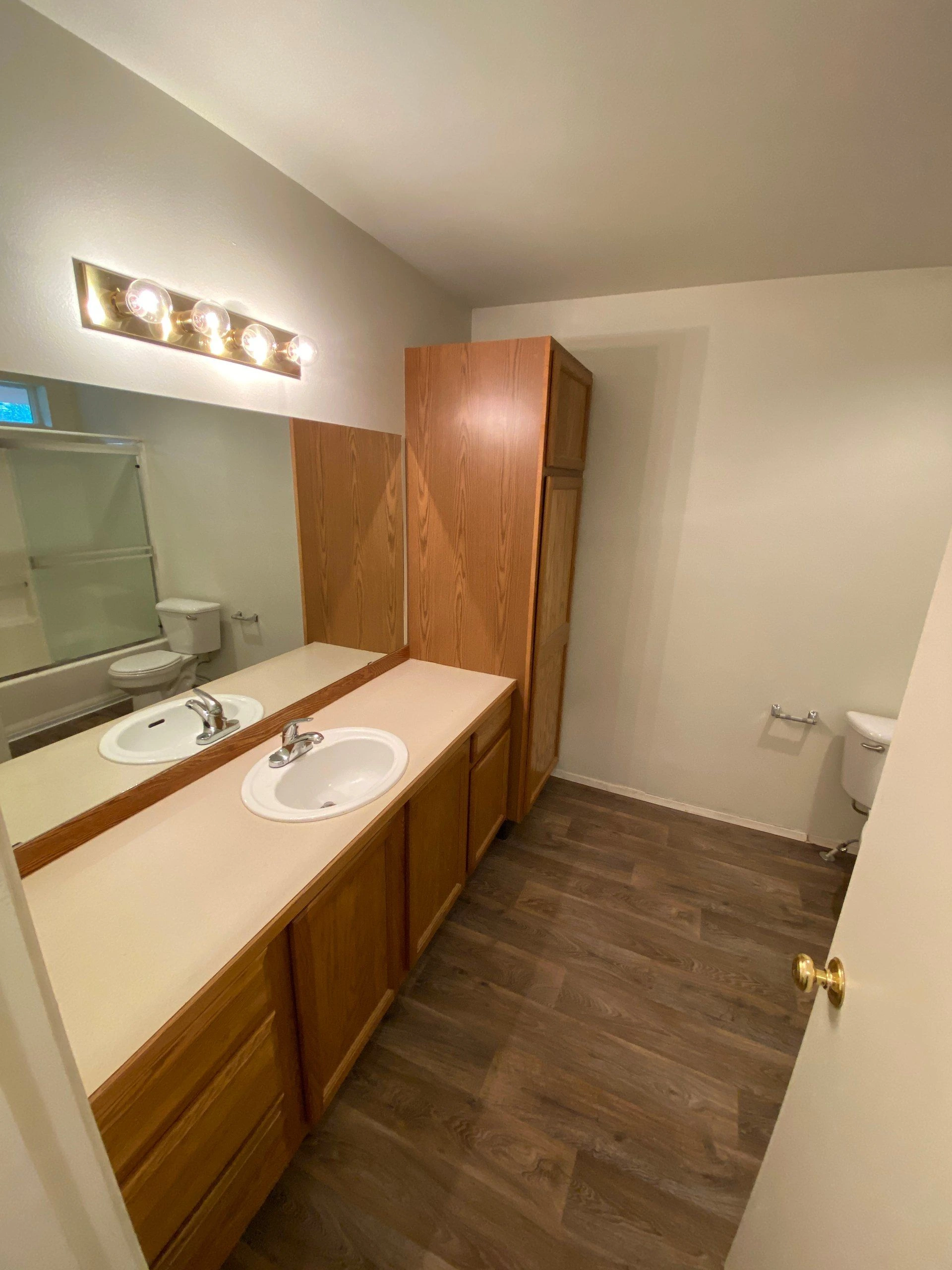 A bathroom with a long wooden vanity, two sinks, a large mirror, a bathtub, and a toilet.