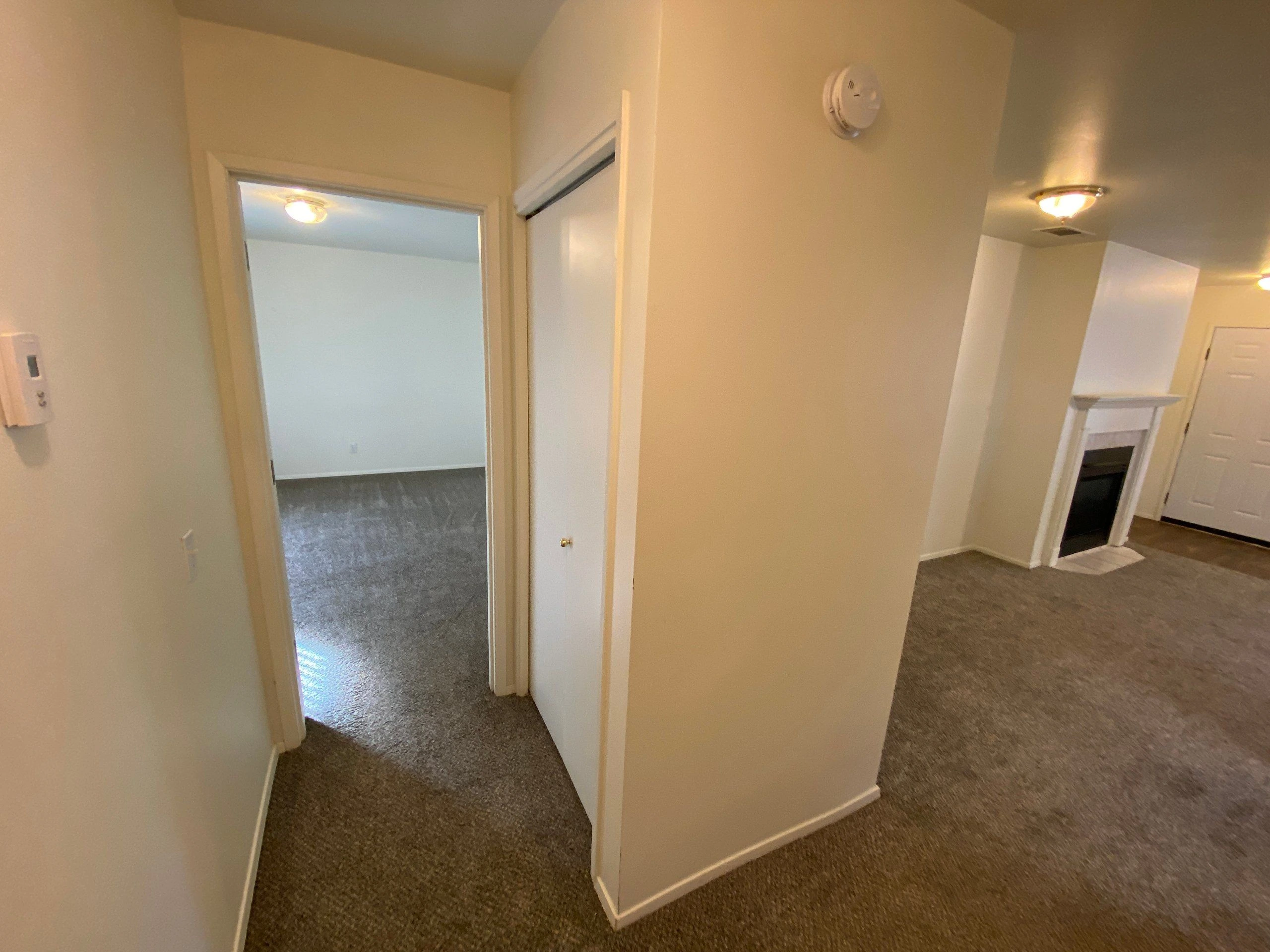 A carpeted hallway has an open doorway to a room, a closed white door, and a fireplace at the far end.