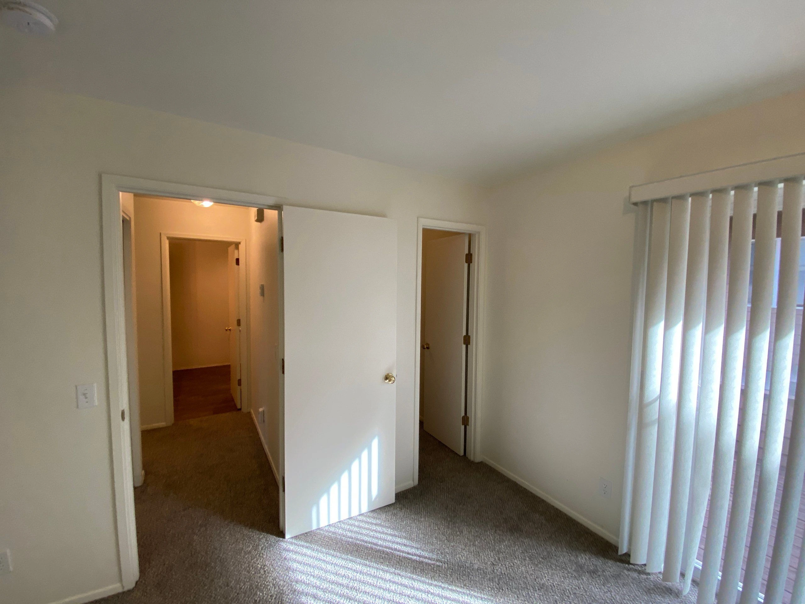 Carpeted room with two open doorways and a window covered by vertical blinds.
