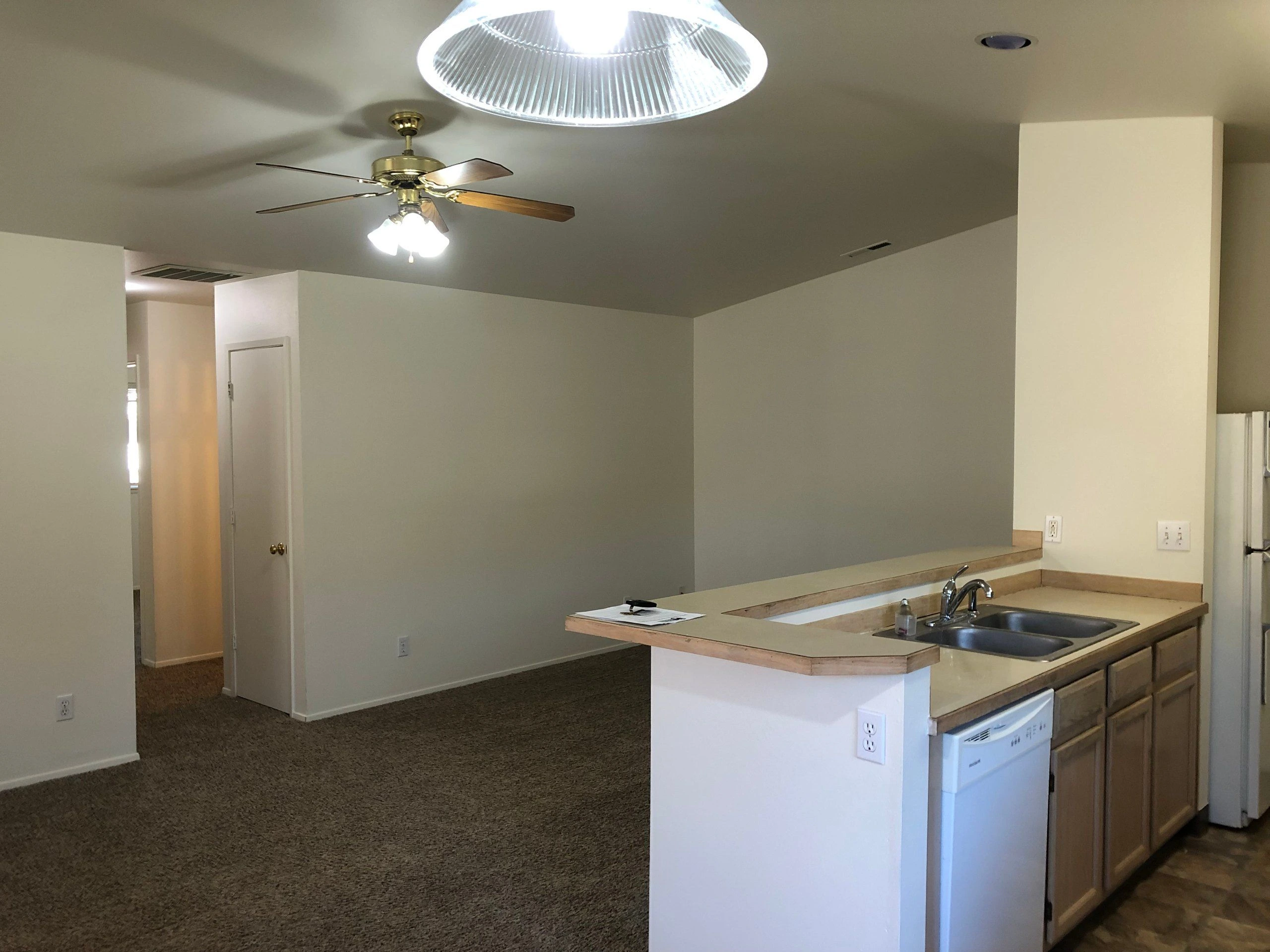 An open kitchen and carpeted living area with a peninsula counter, double sink, wood cabinets, and a ceiling fan.
