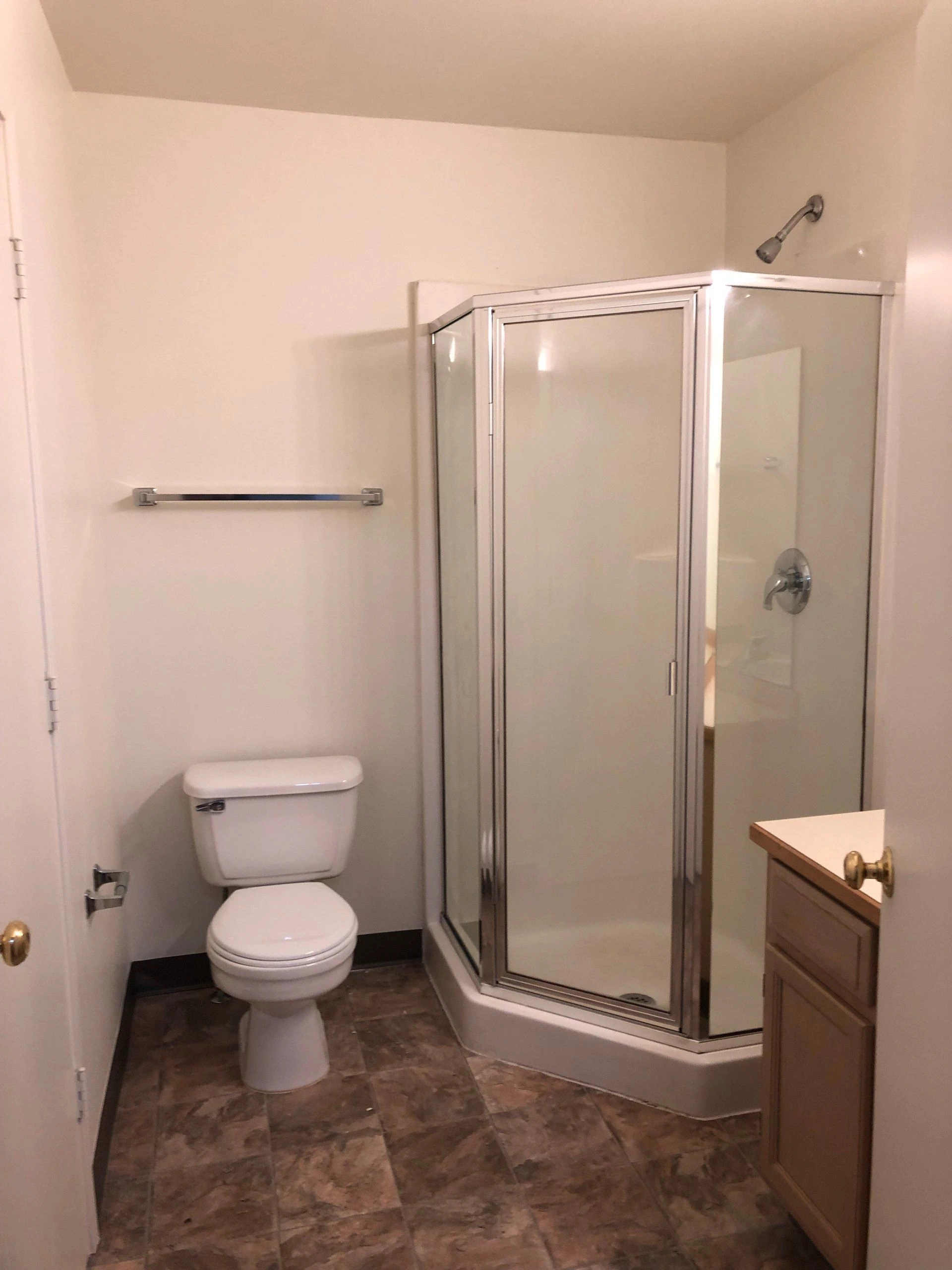 A bathroom with a toilet, a glass-enclosed shower, a towel bar, and a wood vanity.