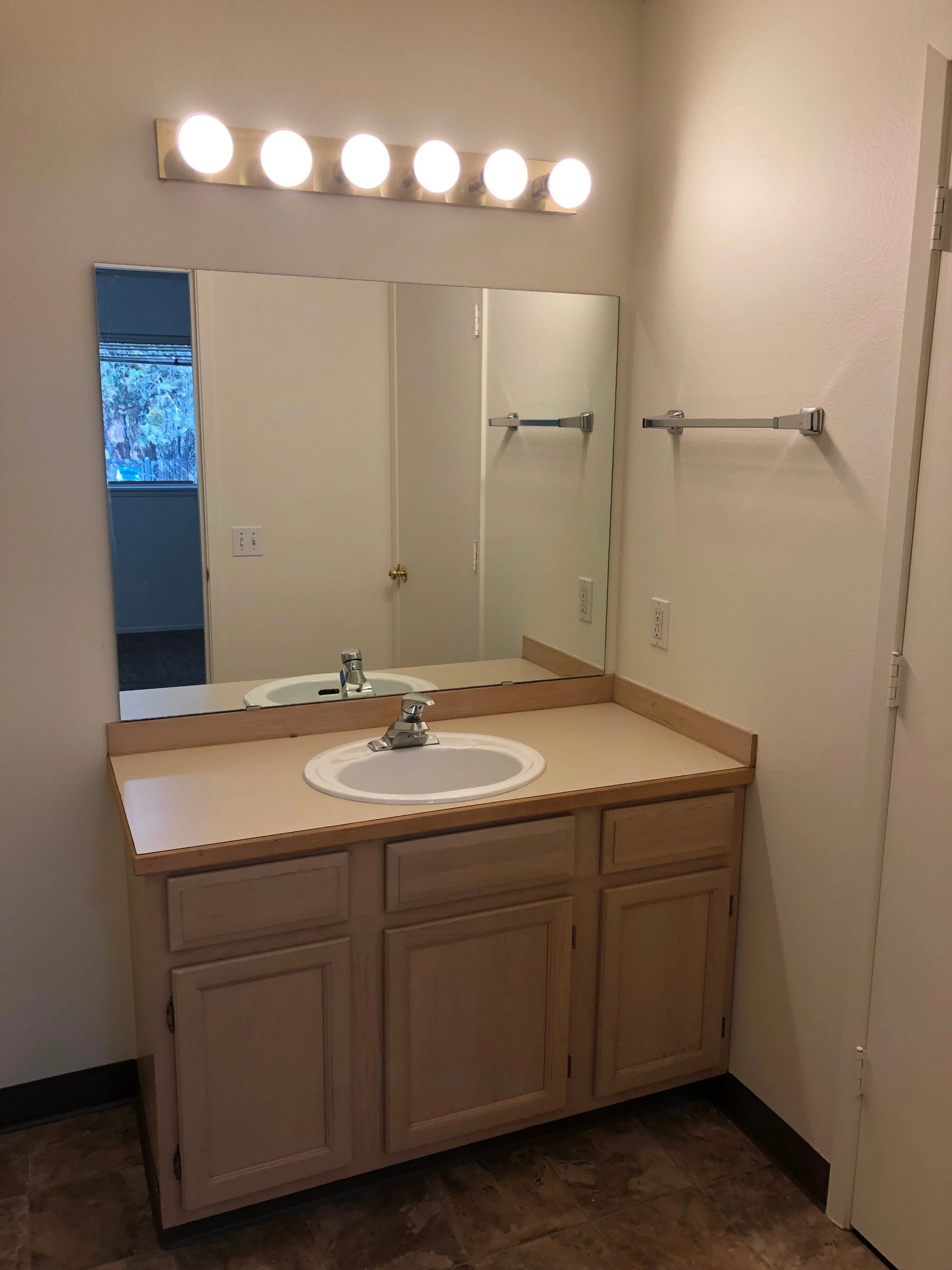 A bathroom vanity with a white sink, wood cabinets, a large mirror, and a row of six lights above it.