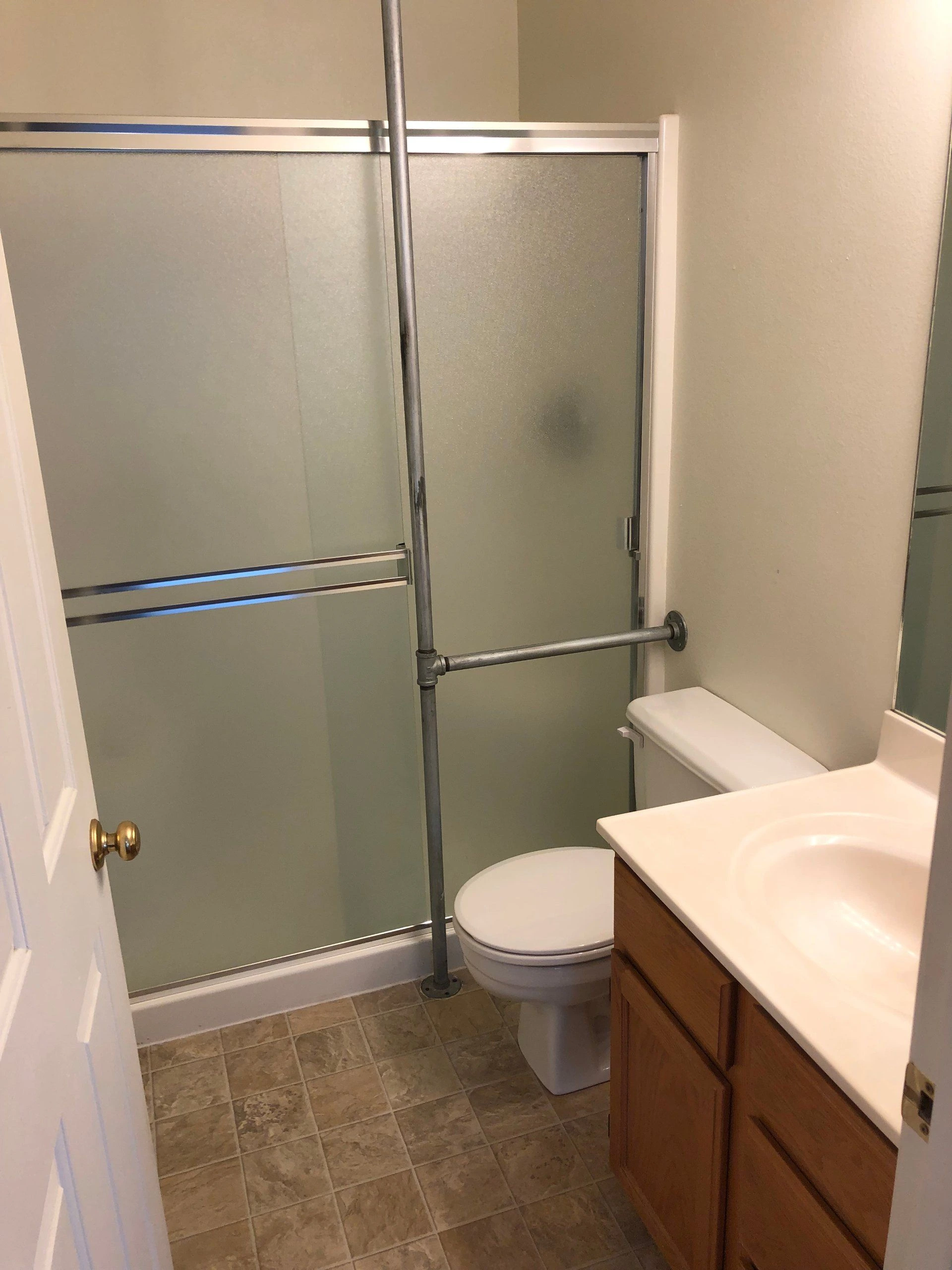 A bathroom with a frosted-glass shower enclosure, toilet, and wood vanity with a white countertop.