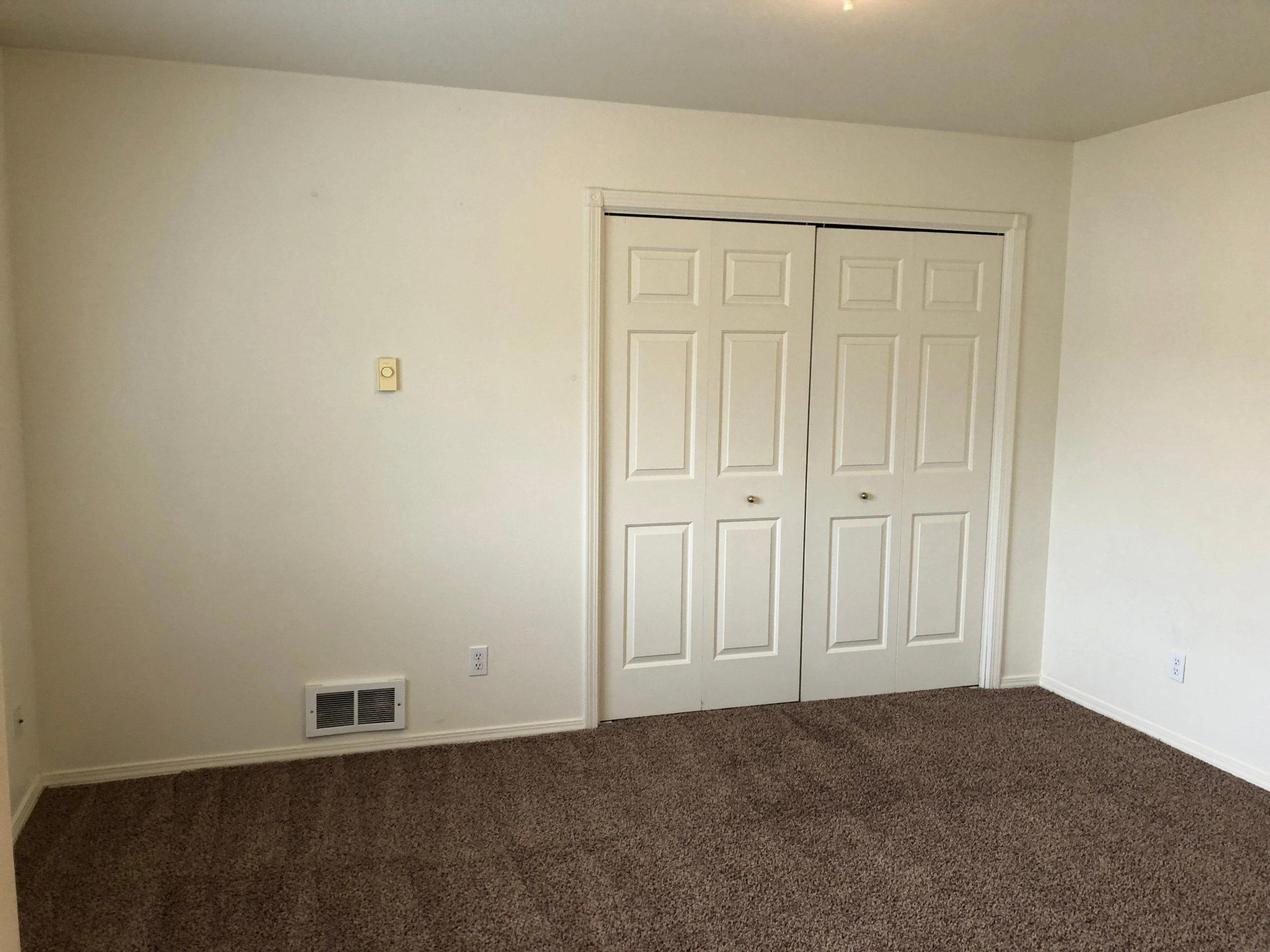 An empty room with brown carpet, cream walls, and closed white paneled closet doors.