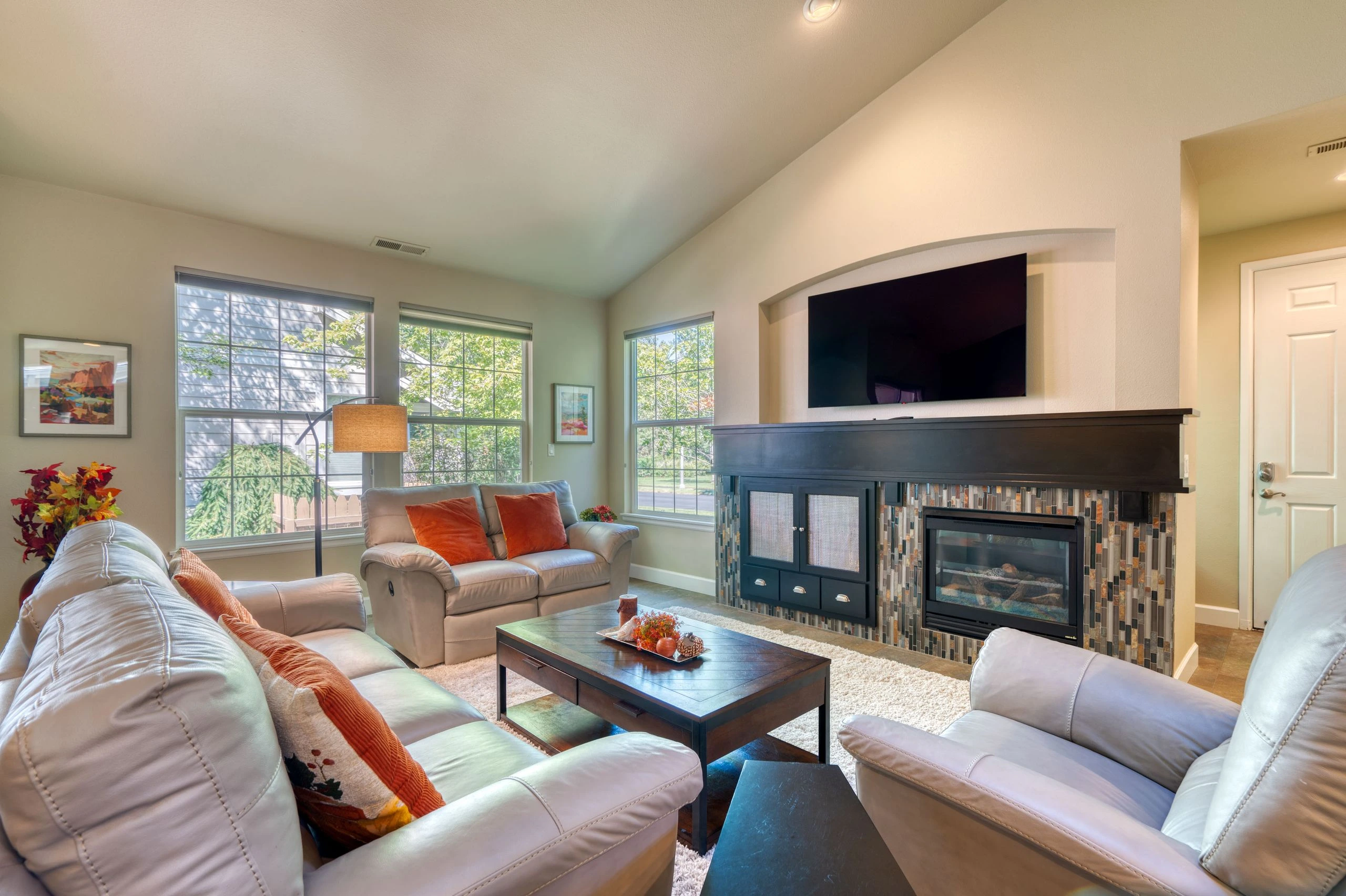 A living room with pale leather sofas, a dark coffee table, and a tiled fireplace with a mounted television.