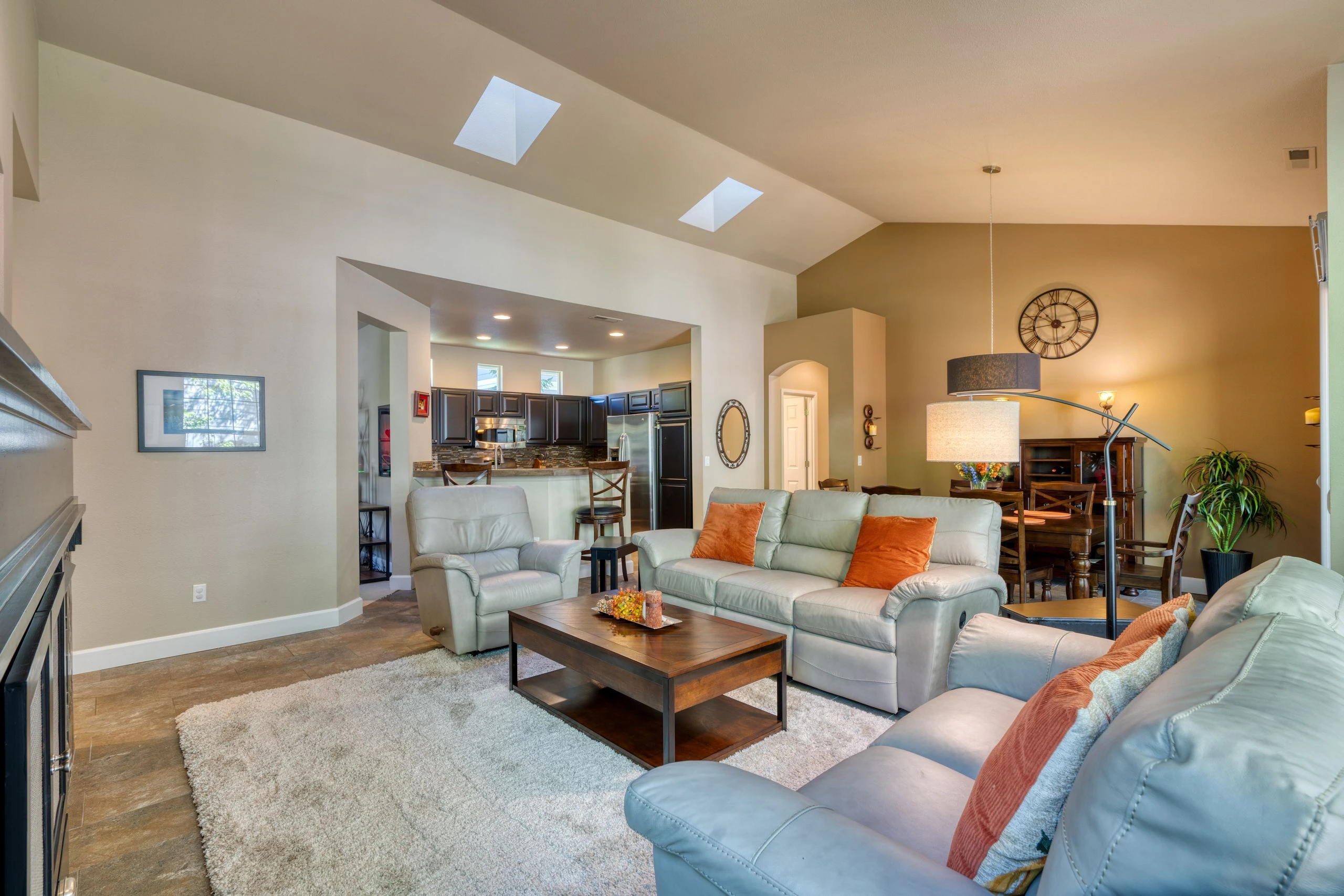 An open living and dining area has pale sofas, a wooden coffee table, a dark-wood kitchen, and two skylights.
