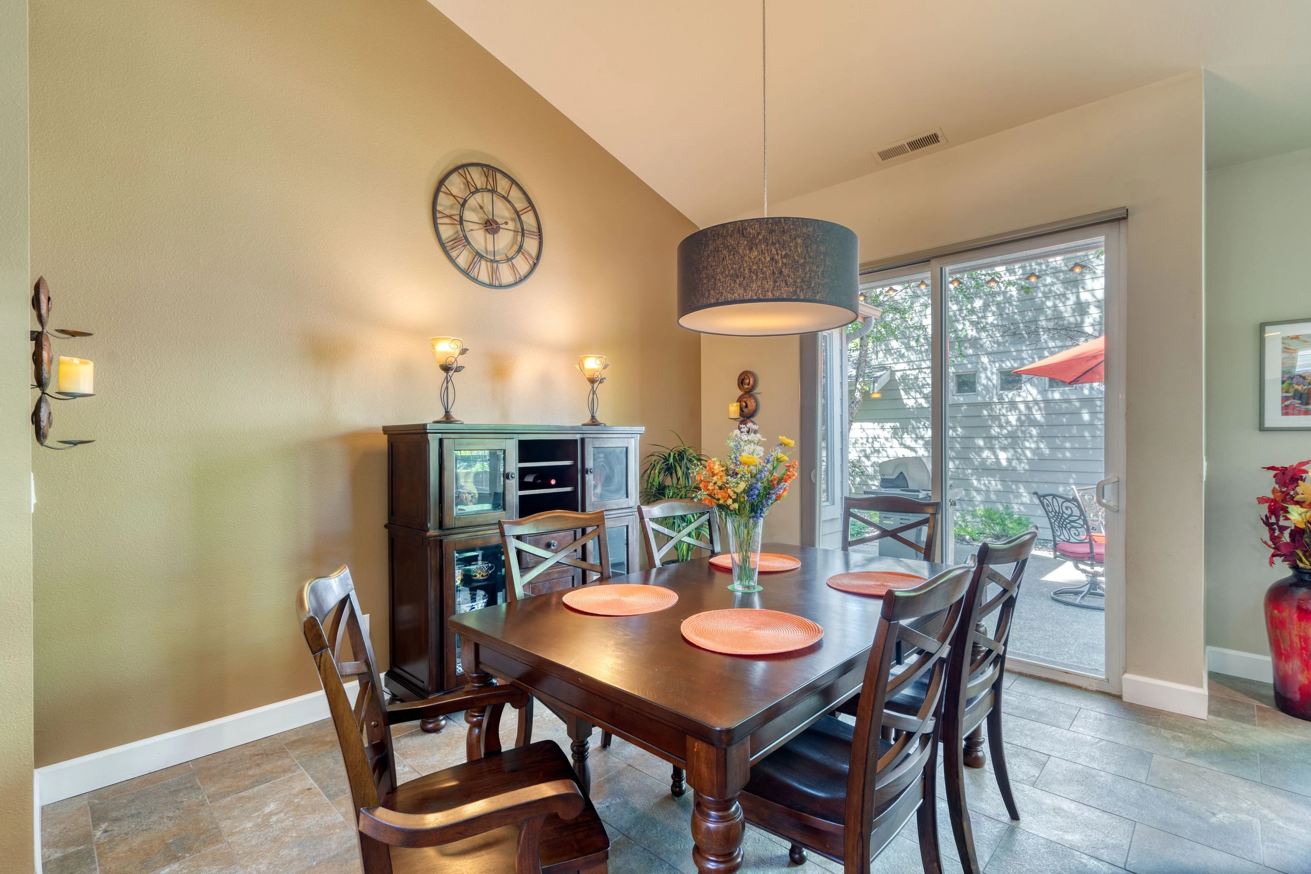 A dark wood dining table and chairs sit beneath a hanging light, beside a glass patio door.