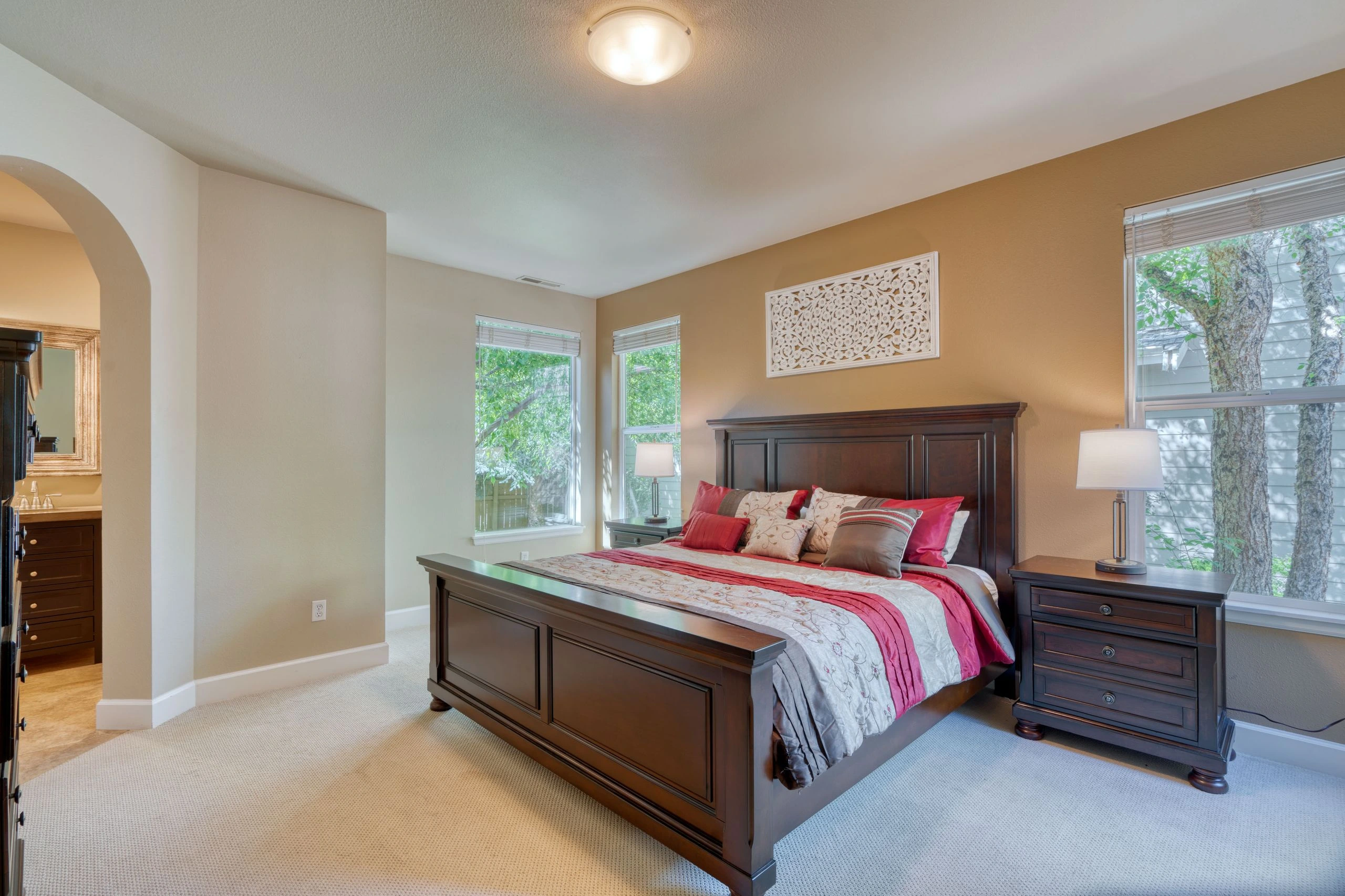 A dark wooden bed with pink and patterned bedding sits between two windows, with matching bedside tables and lamps.