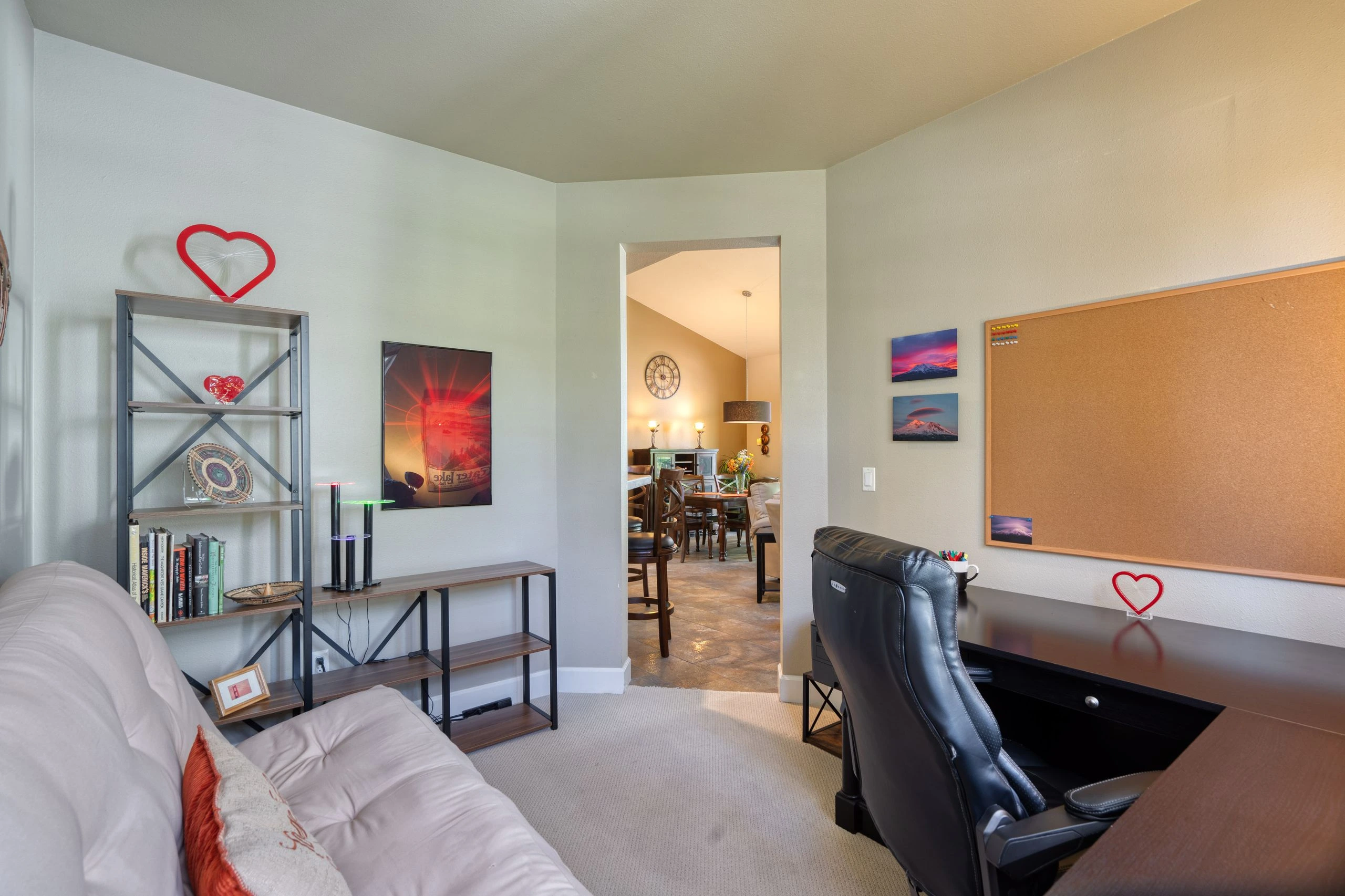 A furnished living room has a light sofa, shelving, a desk and chair, and an open doorway to a dining area.