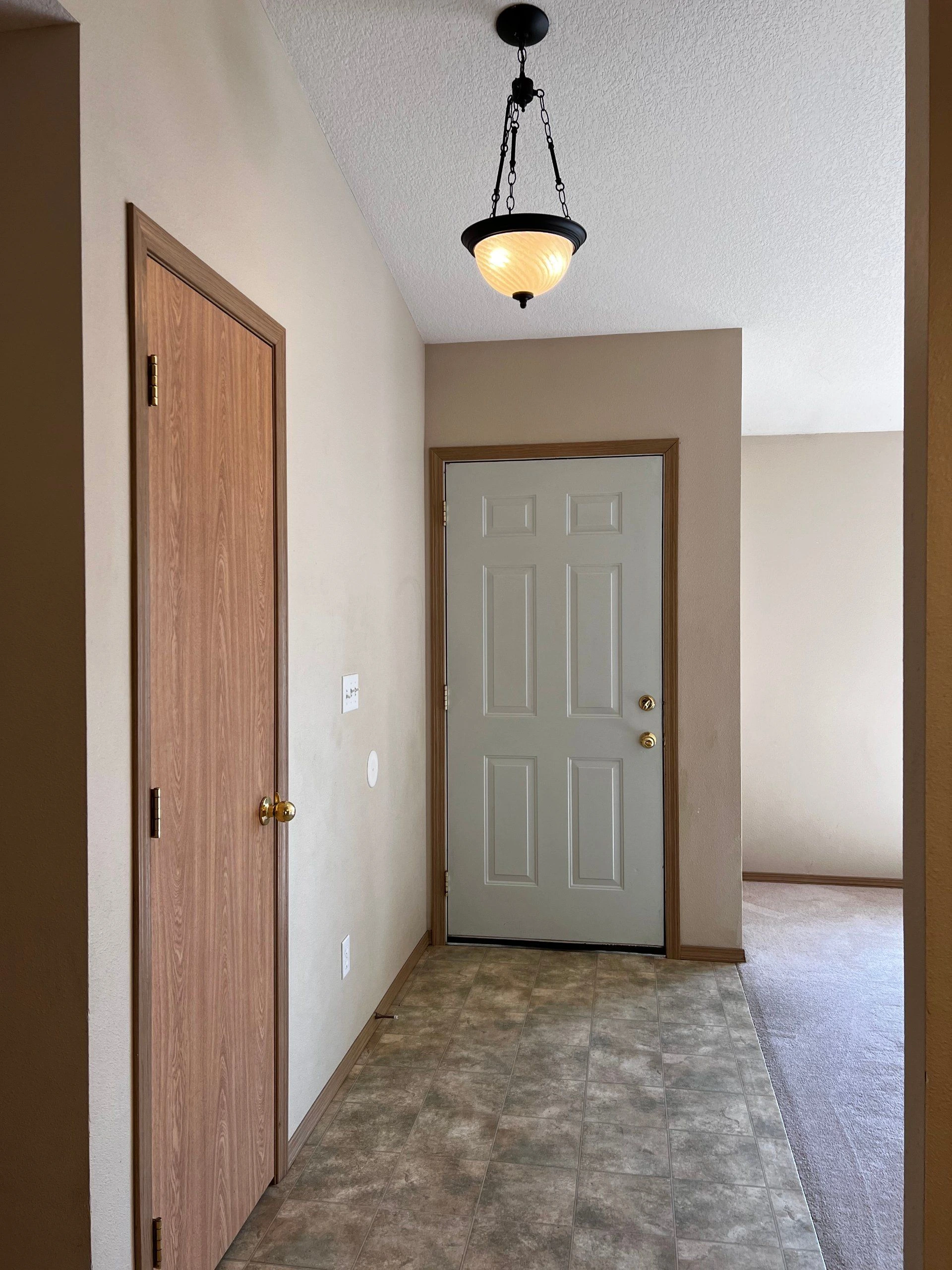 An entryway with a gray paneled door, a wood door, tiled flooring, and a lit hanging ceiling fixture.