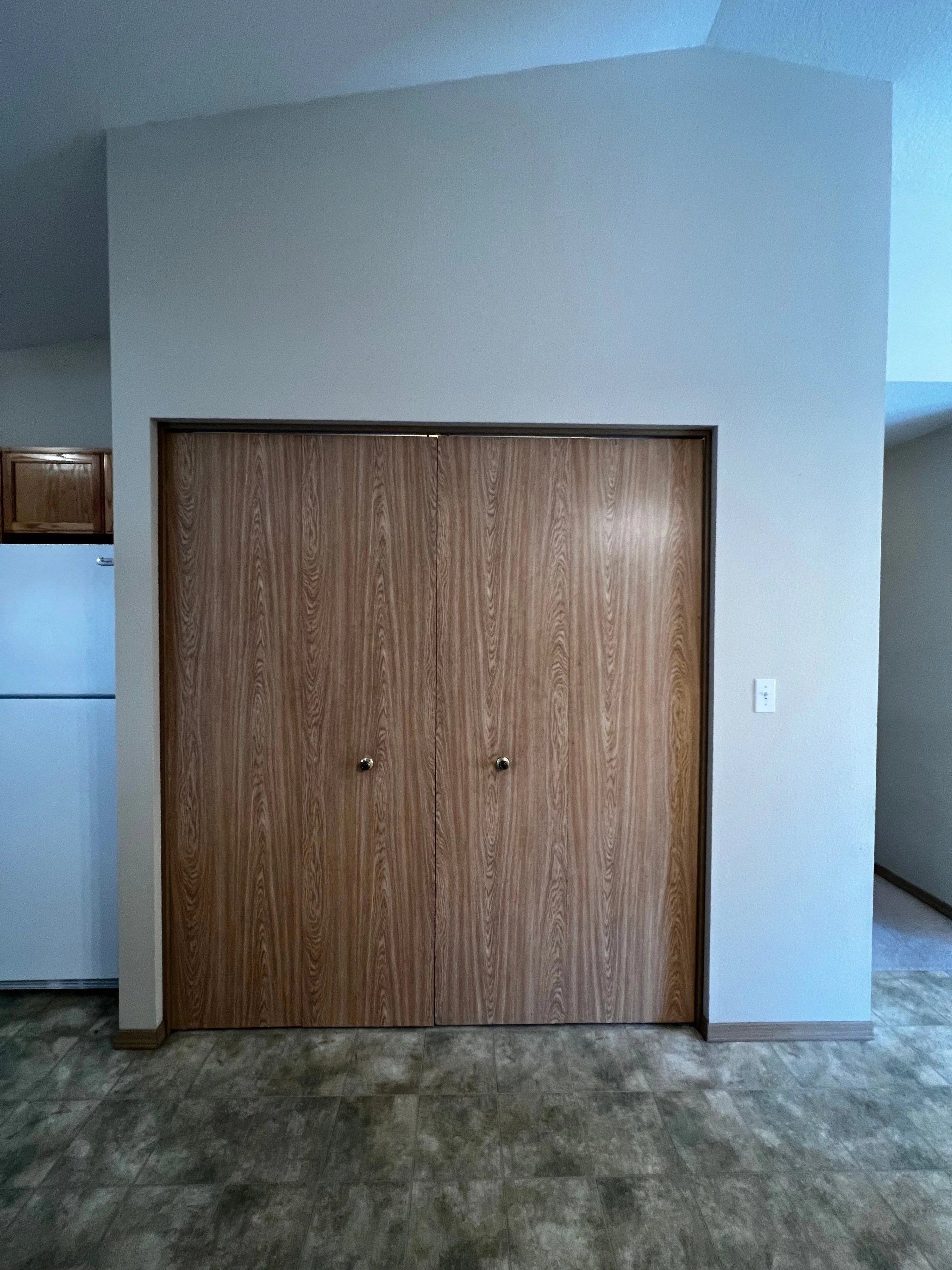 Two closed wood-grain doors stand in a light-colored wall above a gray tiled floor.