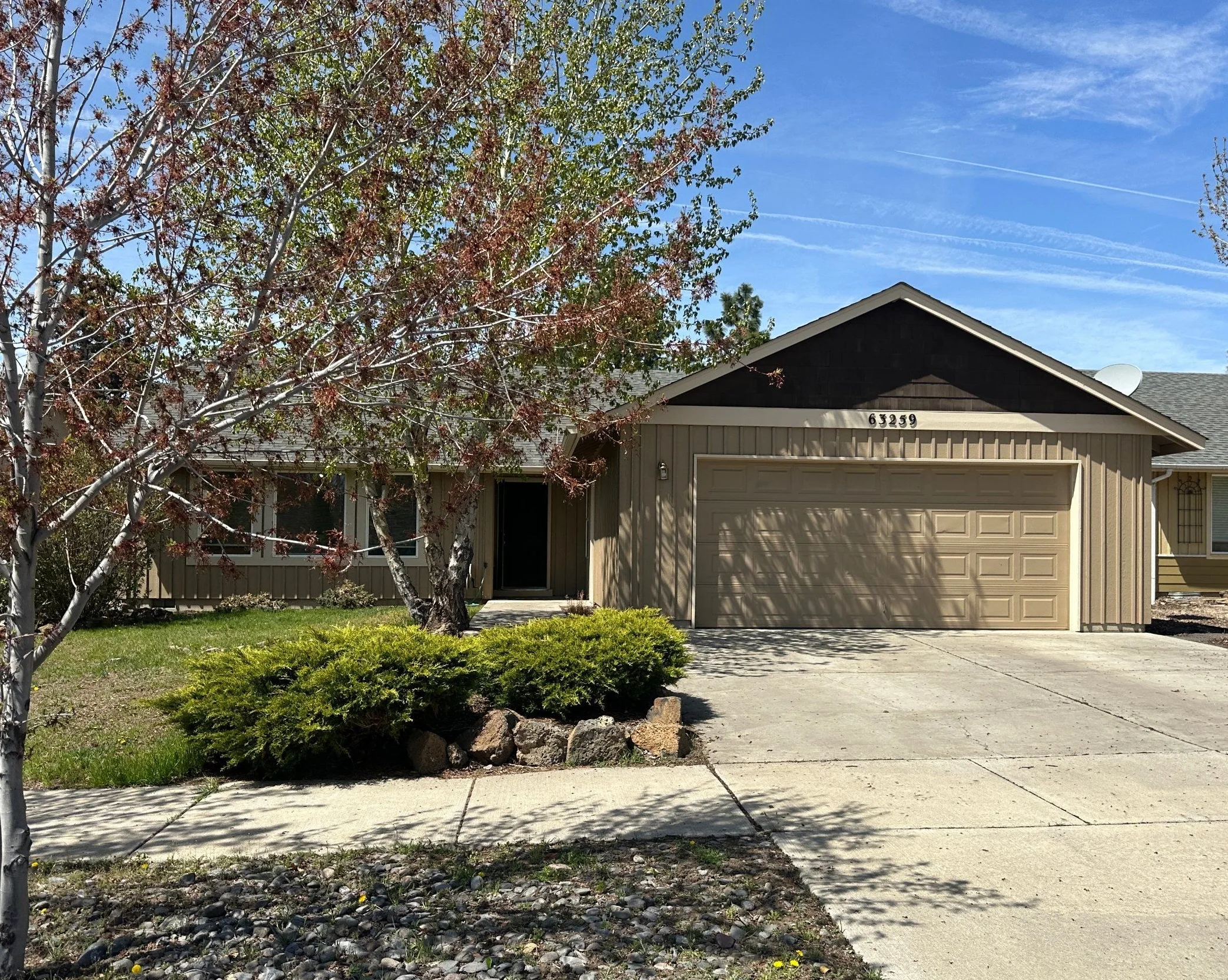 A single-story house with a large garage stands behind a concrete driveway and leafy trees.