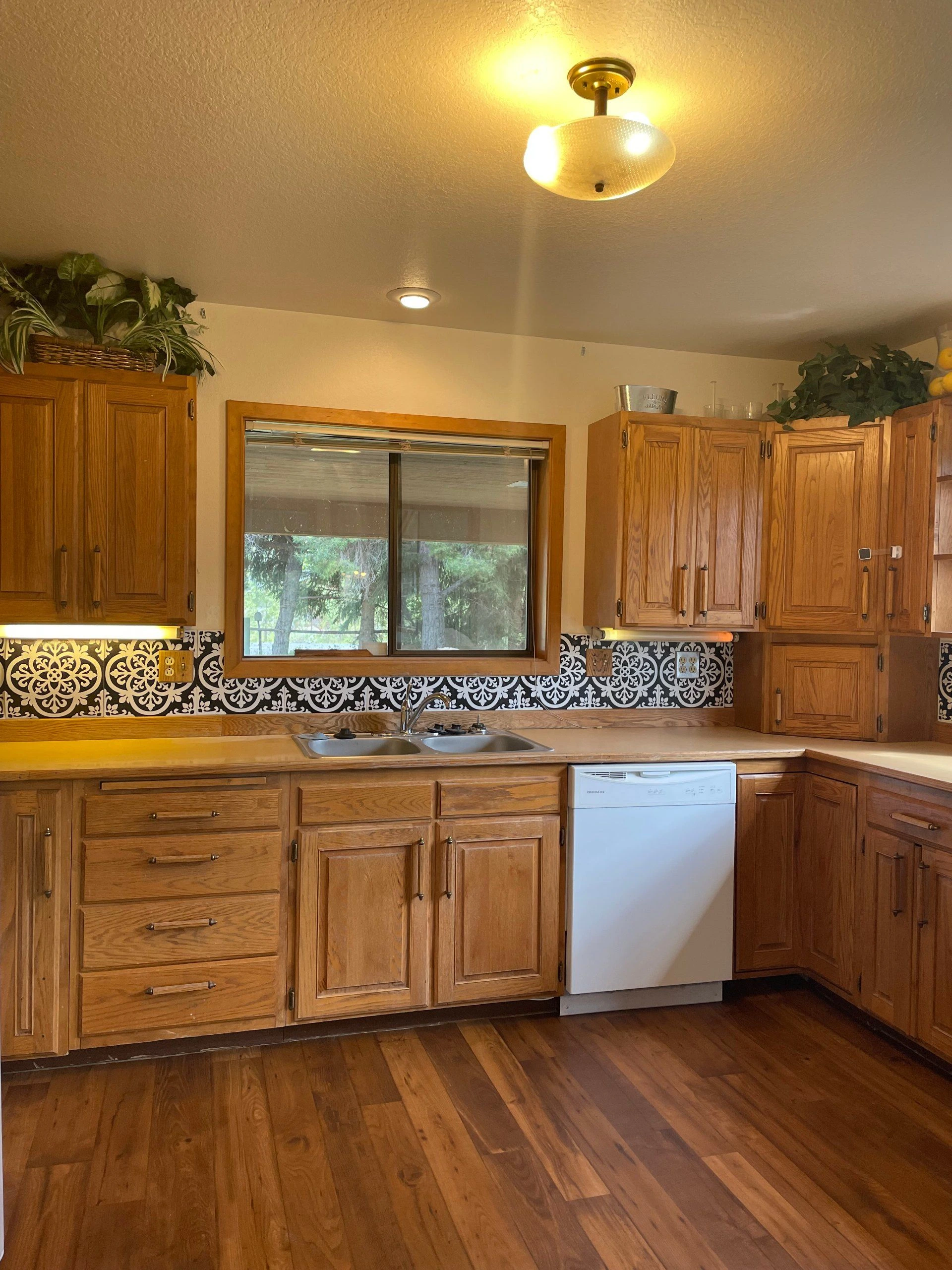 A kitchen with wooden cabinets, a patterned backsplash, a sink beneath a window, and a white dishwasher.