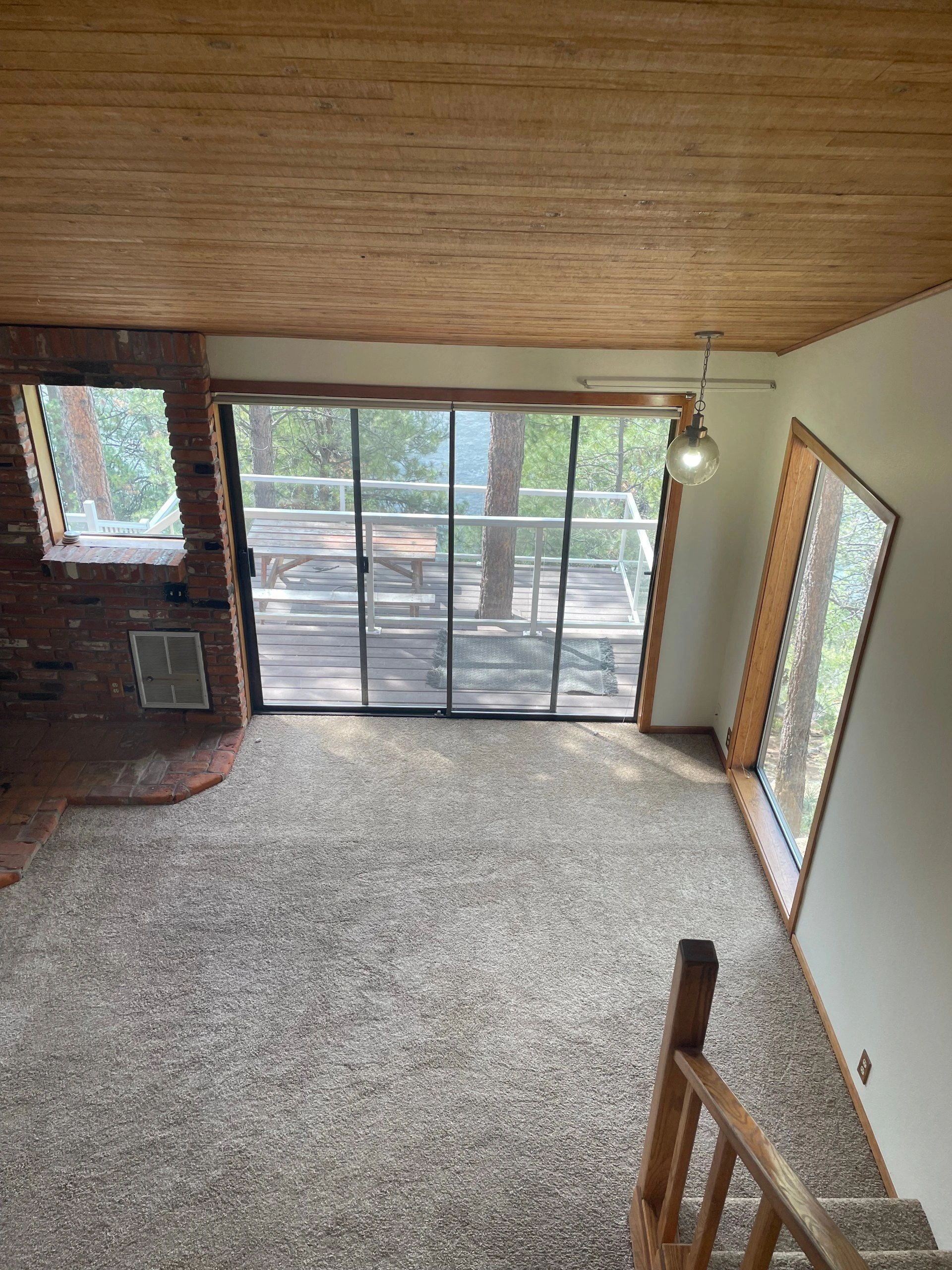 Carpeted room with a brick fireplace, wood-paneled ceiling, and large glass doors opening onto a deck.