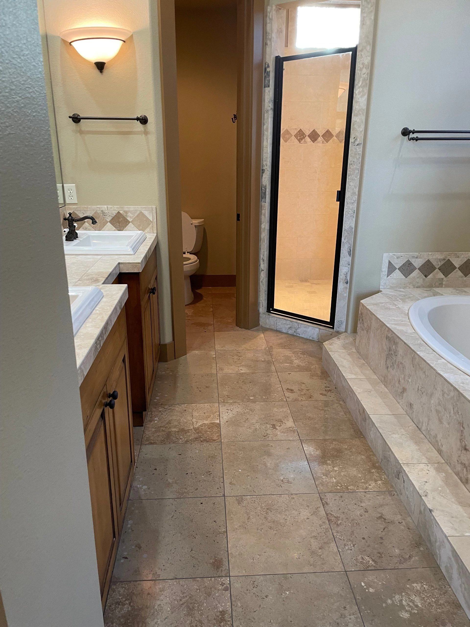 A tiled bathroom has a wood vanity, a toilet in an alcove, a glass shower, and a built-in tub.