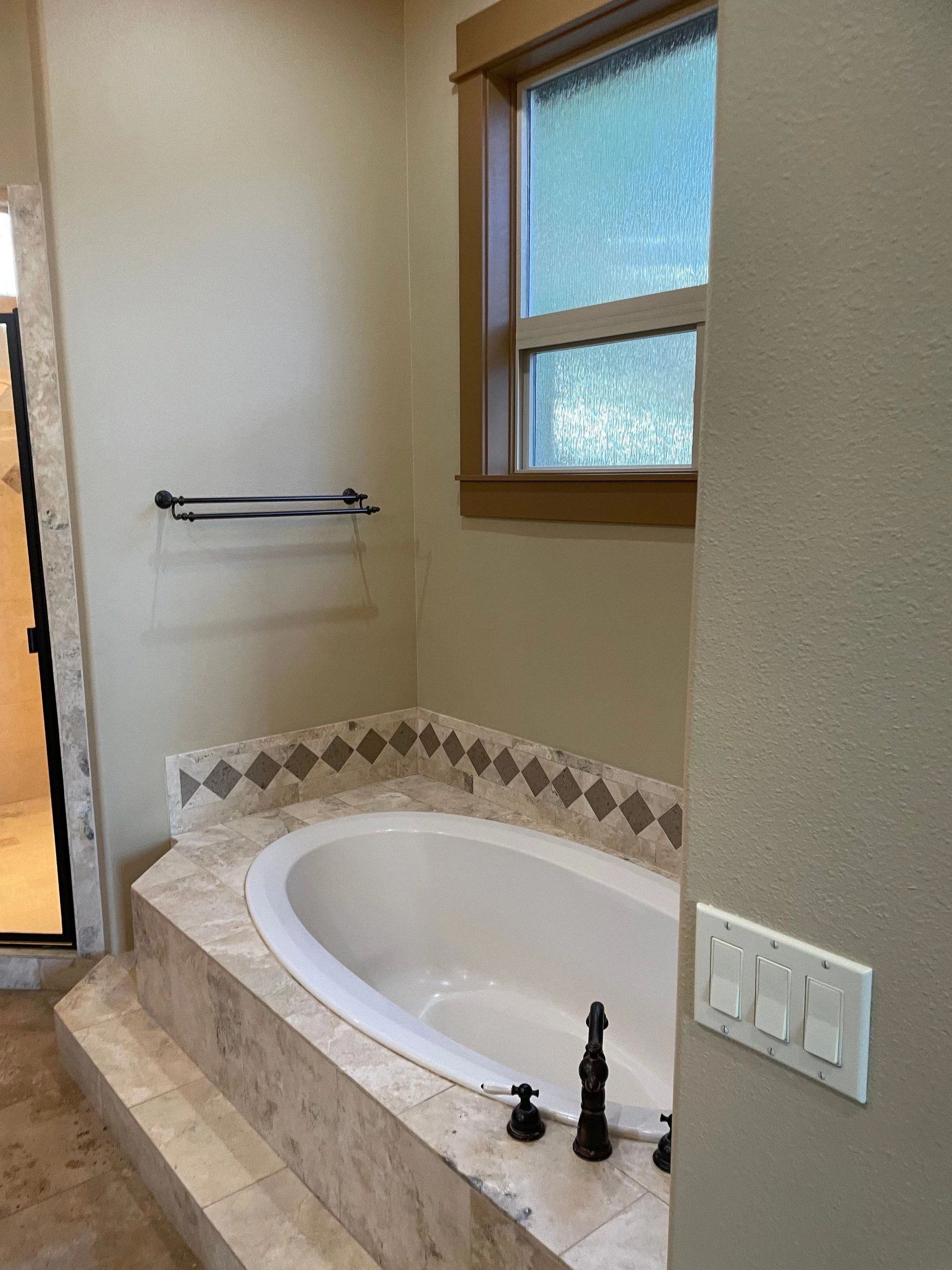 A white oval bathtub set into a tiled platform sits beneath a two-pane frosted window.