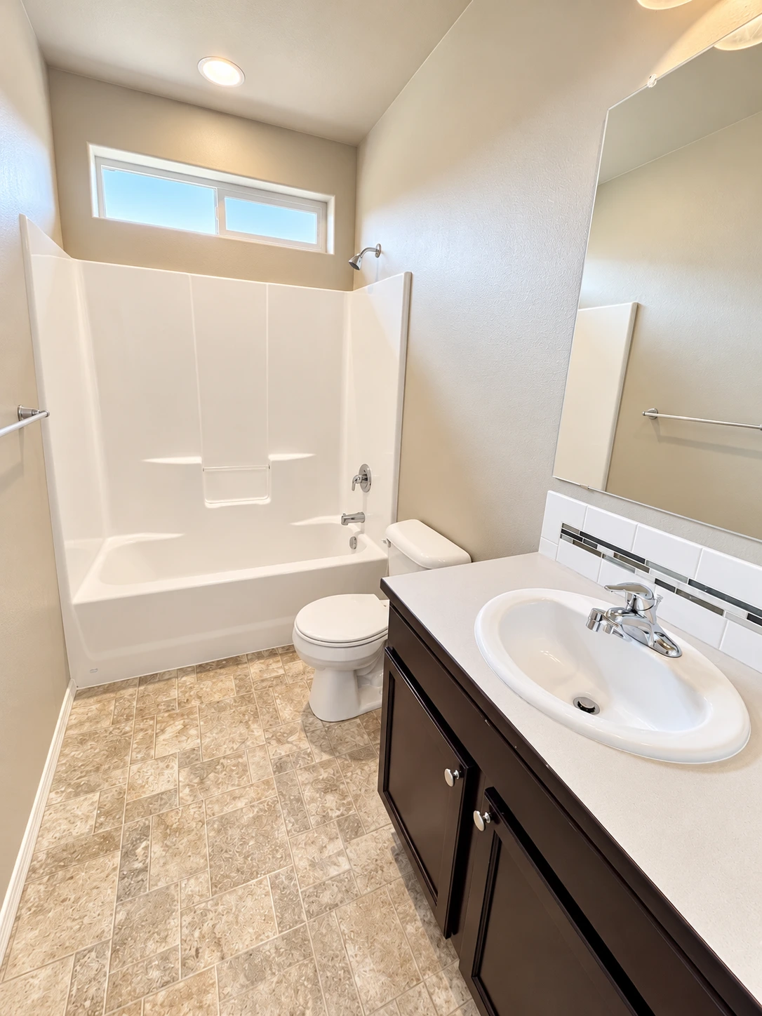 A bathroom with a tub and shower, toilet, dark vanity with an oval sink, large mirror, and patterned tile floor.