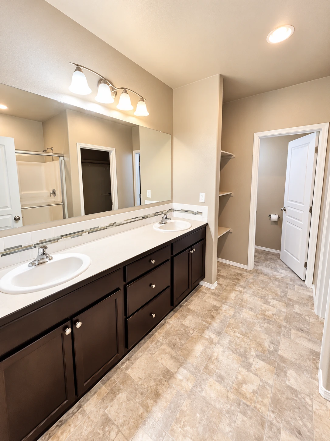 A bathroom with a long dark vanity, two sinks, a large mirror, a shower, and patterned tile flooring.