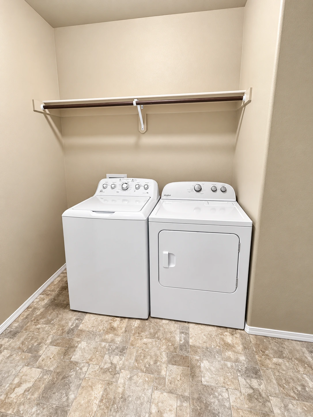 A white top-loading washer and front-loading dryer sit beneath a wall-mounted hanging rod.