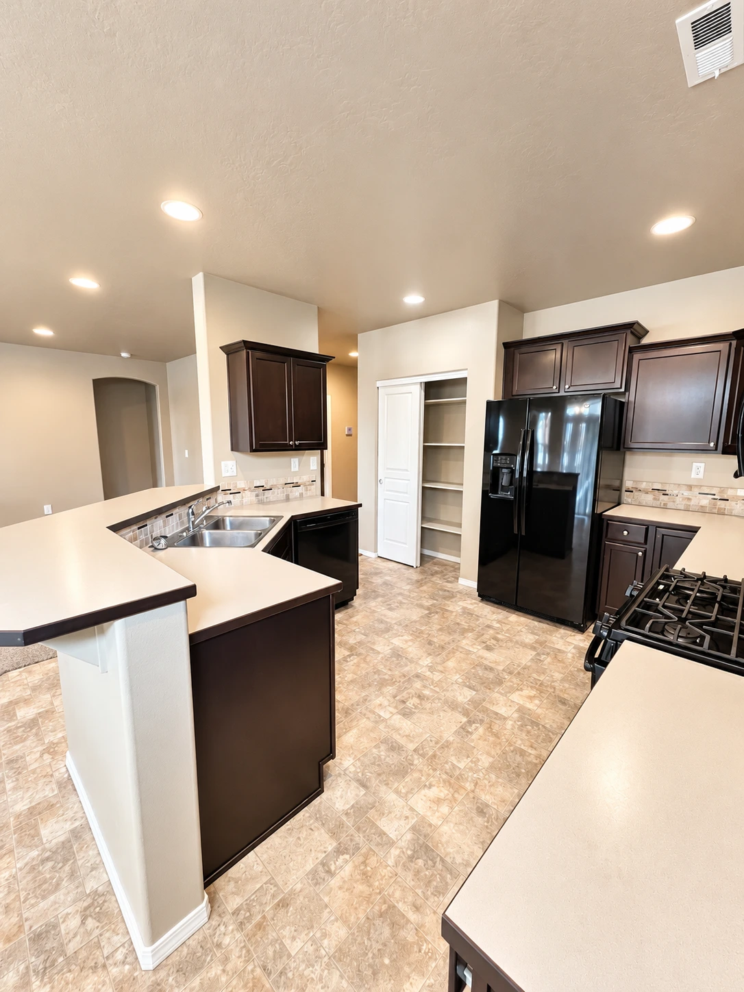 A kitchen with dark cabinets, light counters, a double sink, black refrigerator and range, and patterned tile flooring.