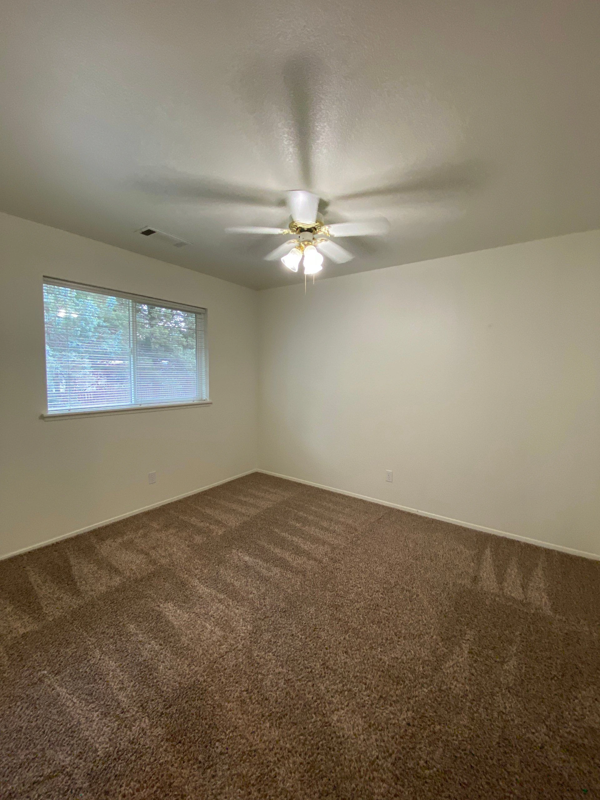 An empty carpeted room with a ceiling fan with lights and a window.