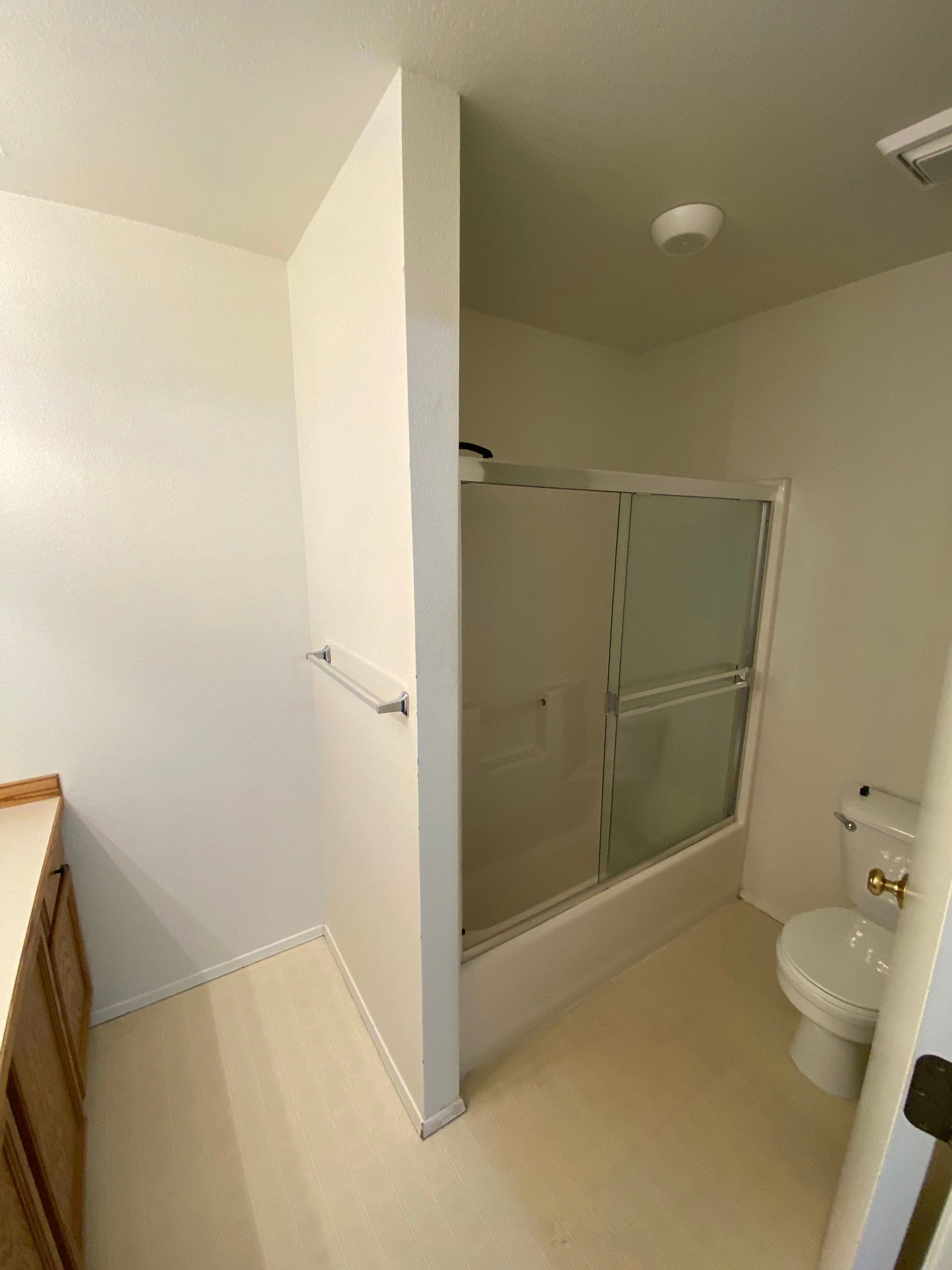 A bathroom with a glass-panel tub and shower, a toilet, a towel bar, and part of a wooden vanity.