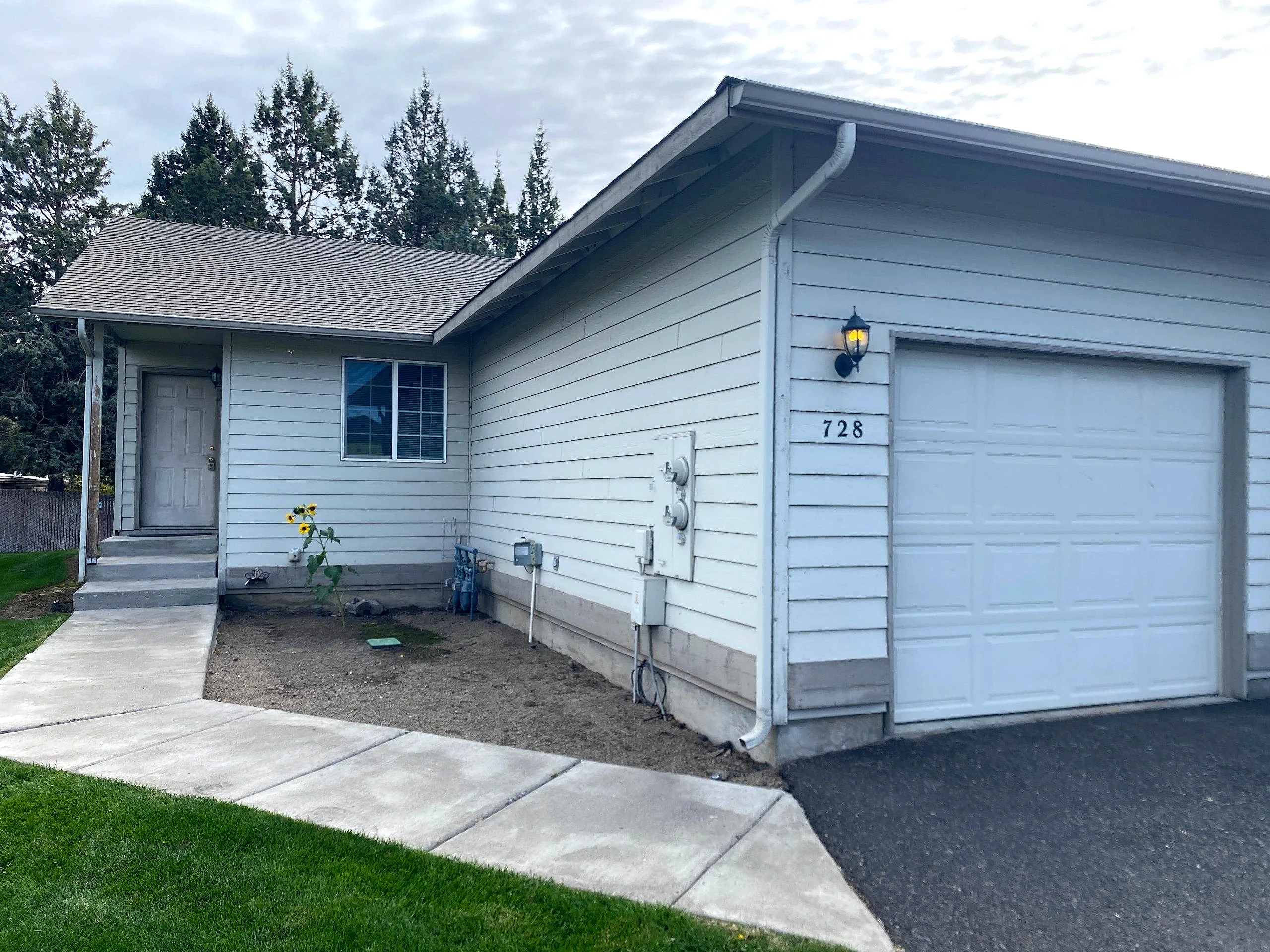A light-sided house with a large garage door, front entry, window, and concrete walkway.