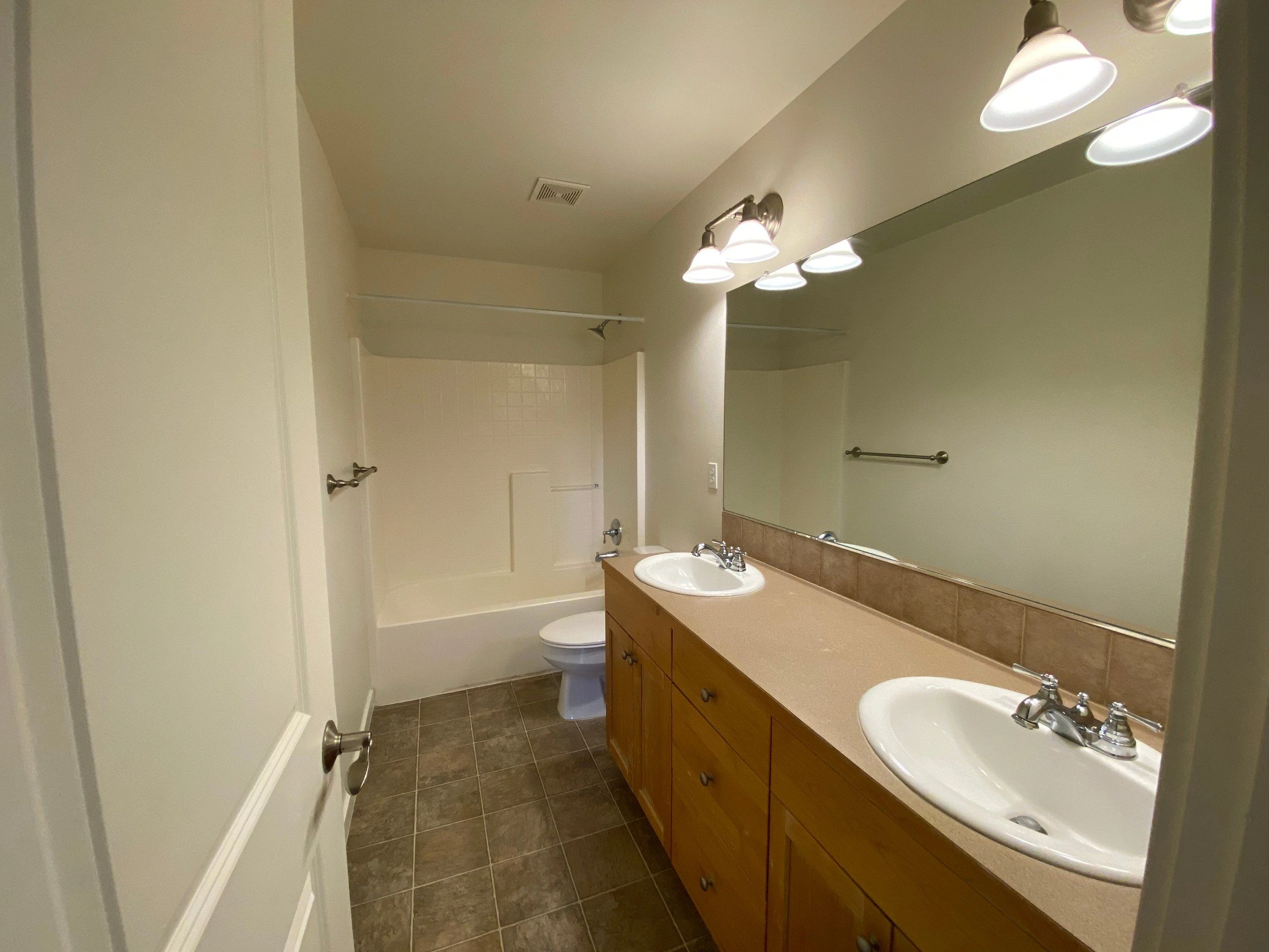 Bathroom with a long wooden vanity and two sinks, a large mirror, a tub-shower, and a tiled floor.