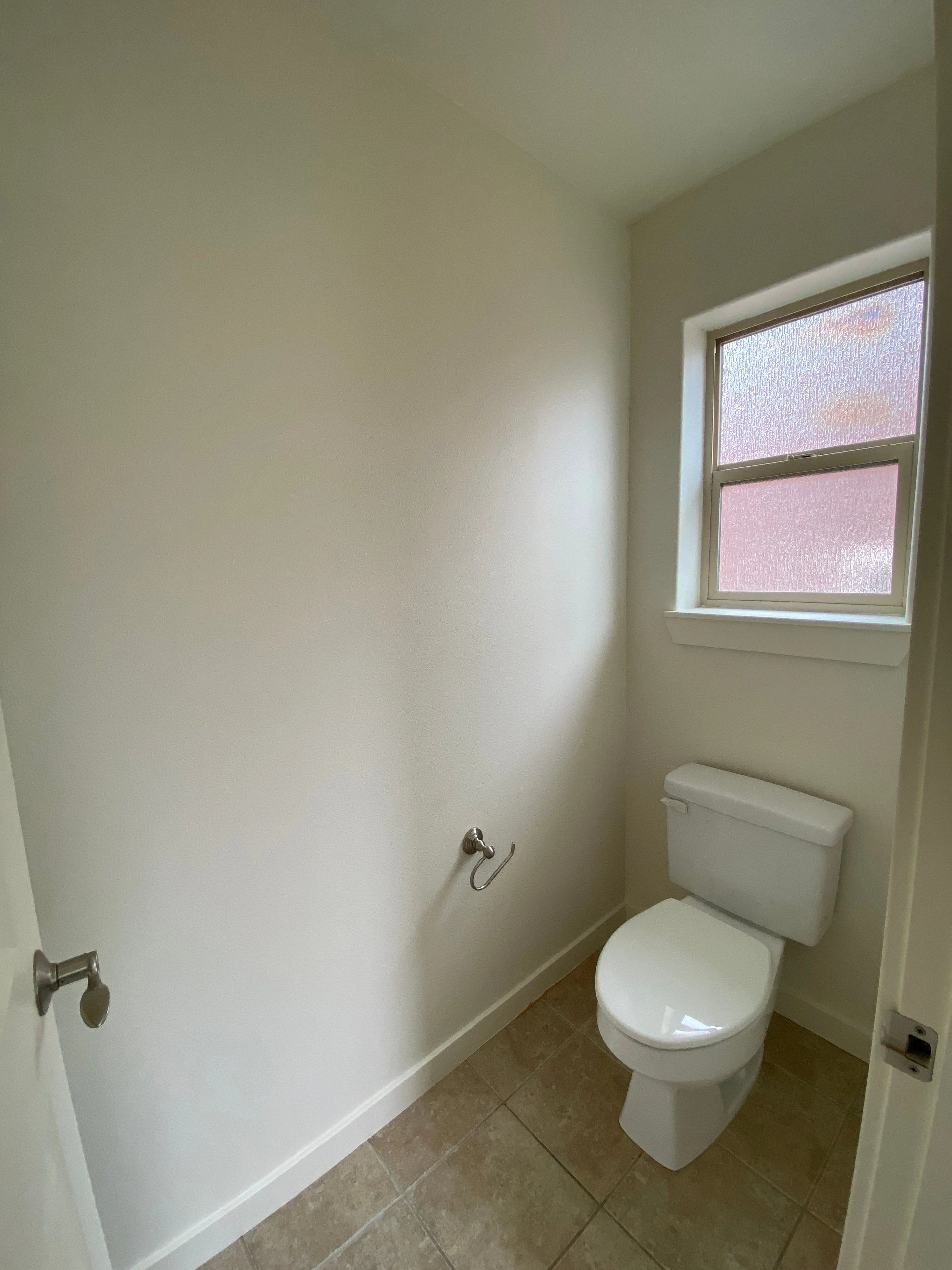 A white toilet sits beneath a textured-glass window in a small room with tiled flooring.