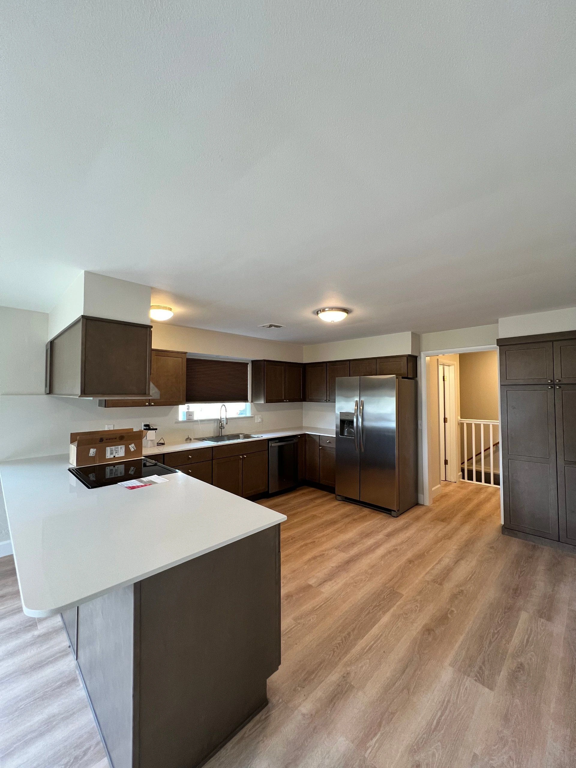Kitchen with a white island, dark cabinets, stainless steel appliances, and wood-patterned flooring.