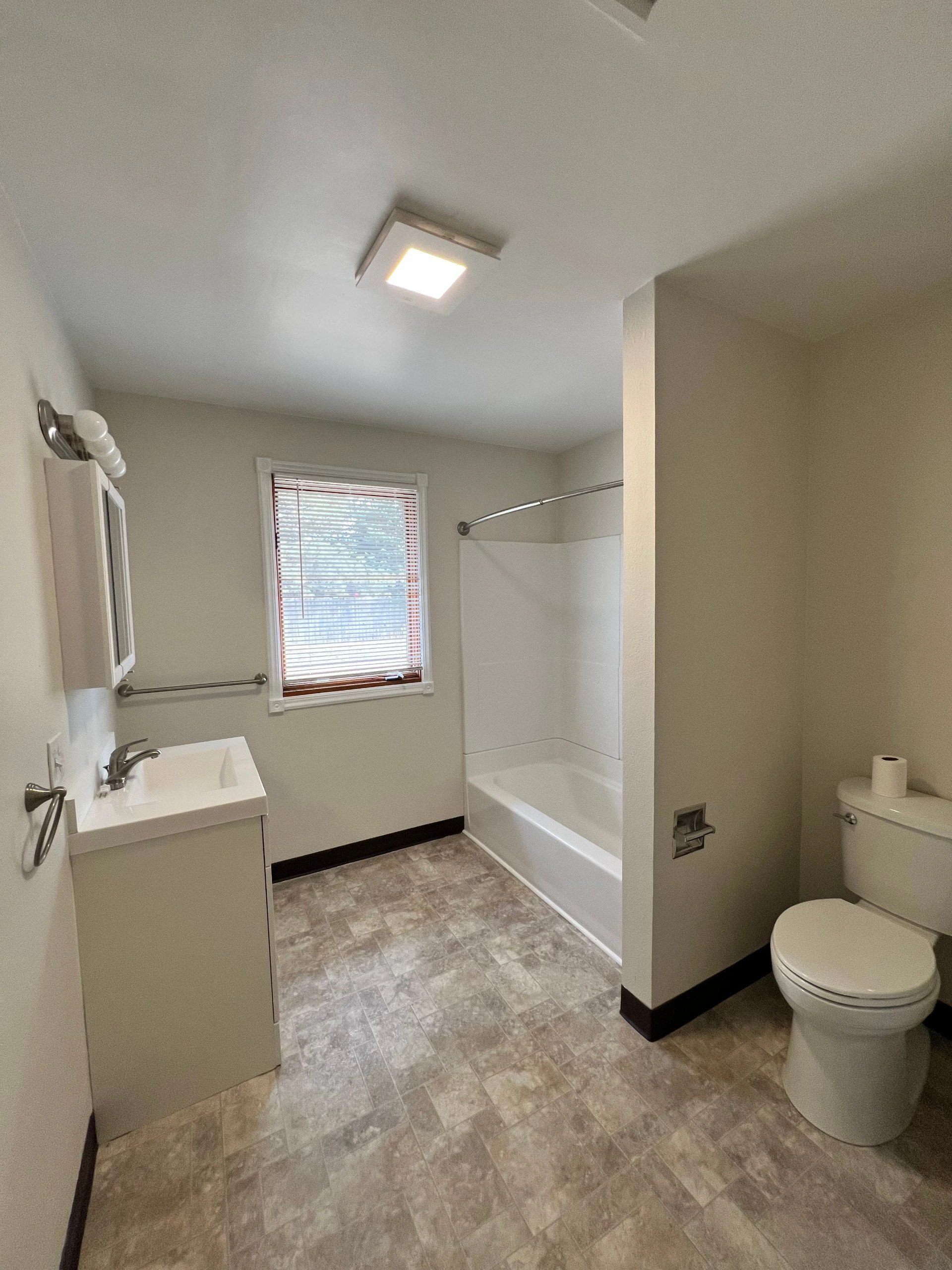 A bathroom with a sink, bathtub and shower, toilet, and a window with blinds.