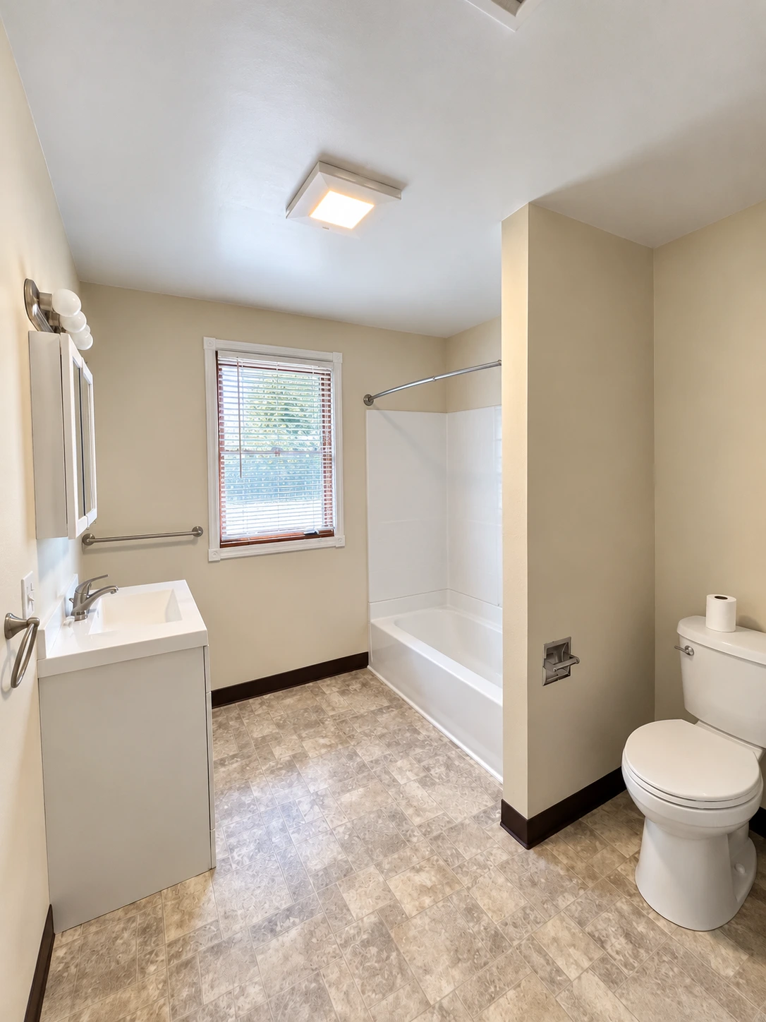 A bathroom with a sink and mirrored cabinet, a window with blinds, a bathtub, and a toilet.