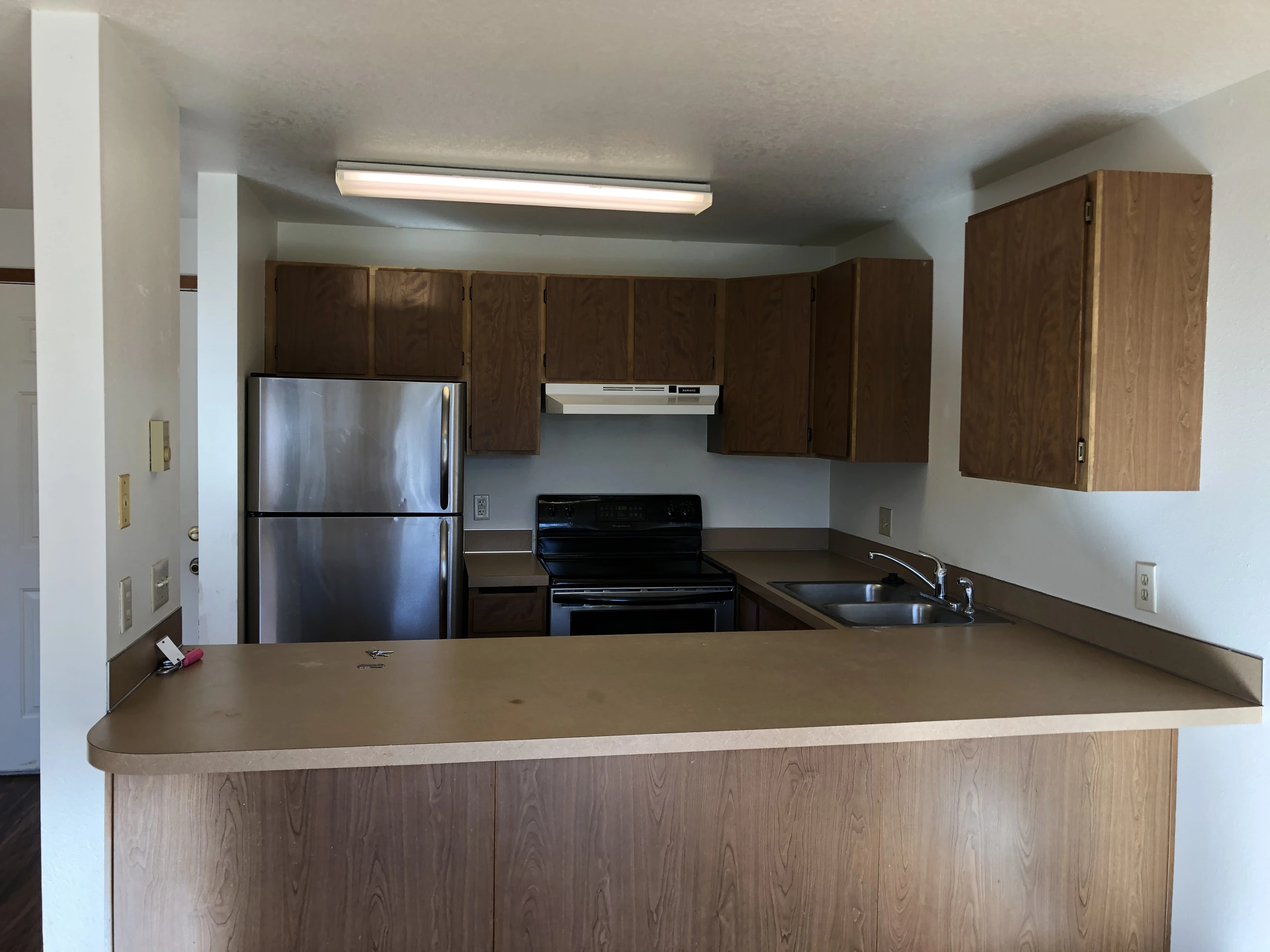 Kitchen with wood cabinets, a refrigerator, stove, range hood, sink, and a large peninsula countertop.