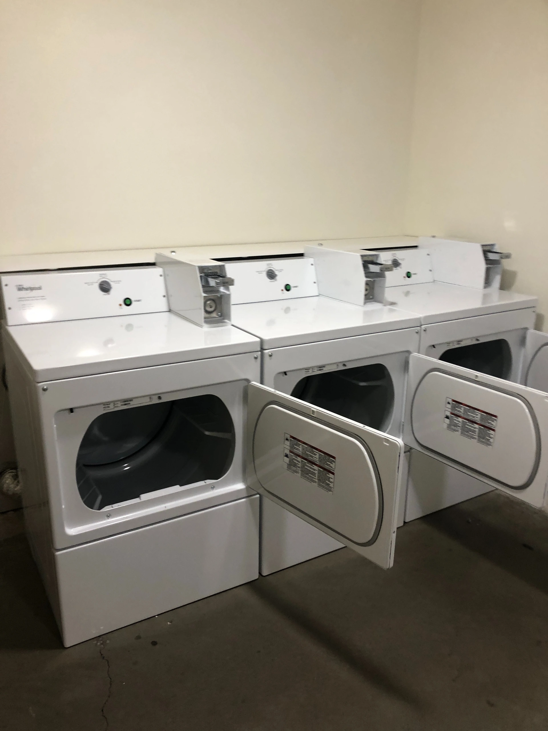 Three white front-loading laundry machines with open doors are lined up against a wall.