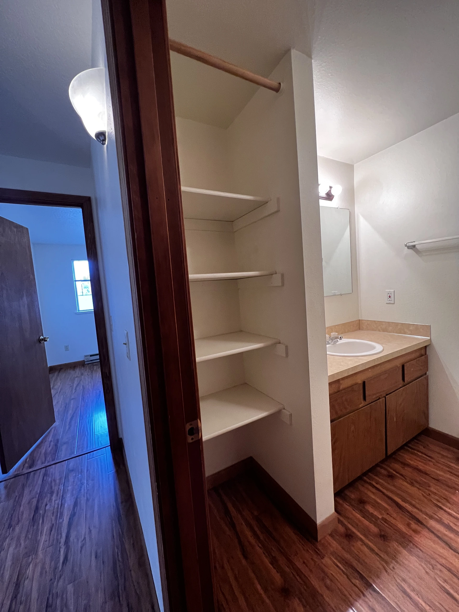 Bathroom vanity with sink, mirror, wooden cabinets, towel bar, and built-in shelves beside an open doorway.