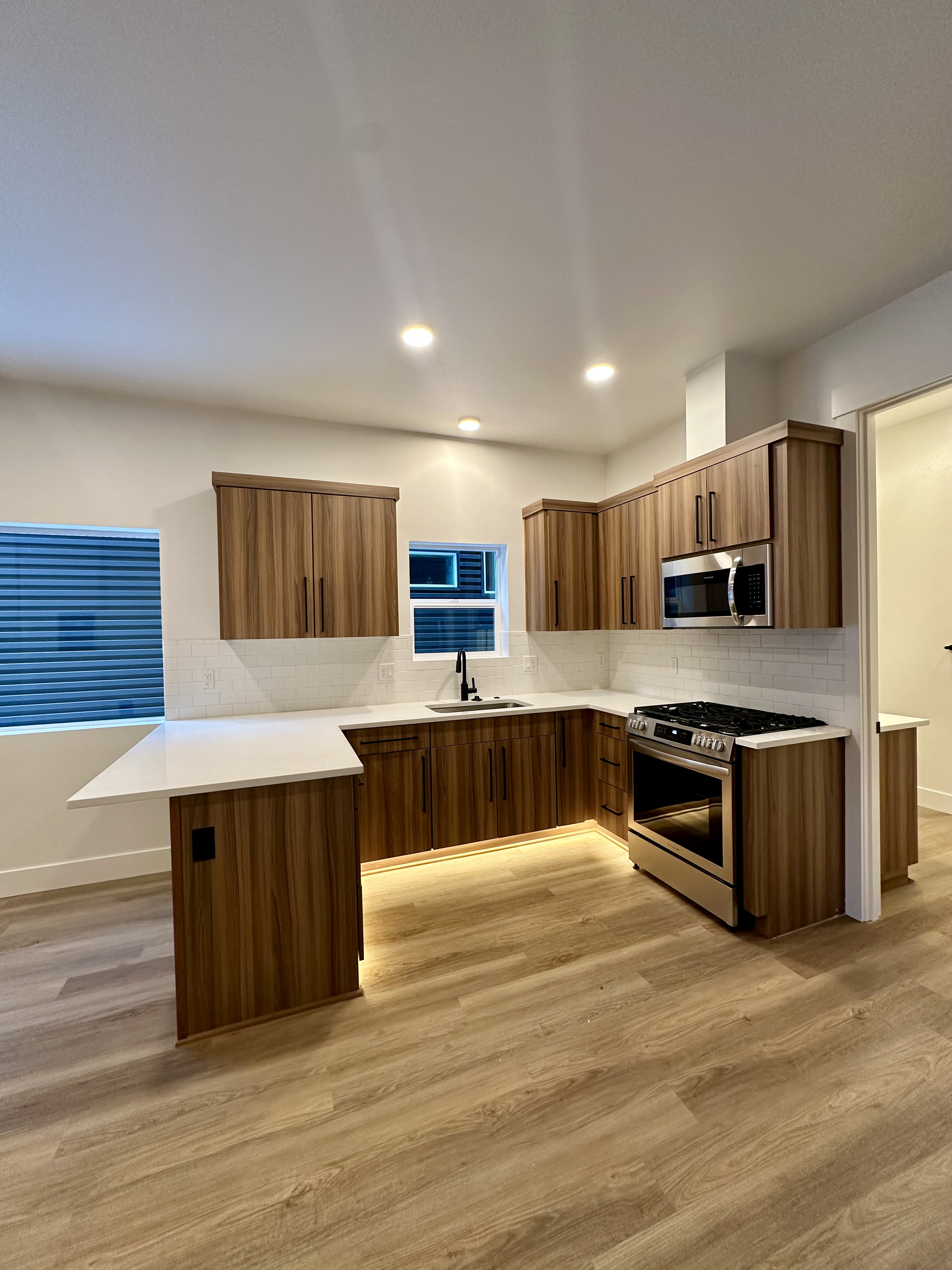 Kitchen with wood cabinets, white counters, tiled backsplash, windows, recessed lights, sink, microwave, and gas range.